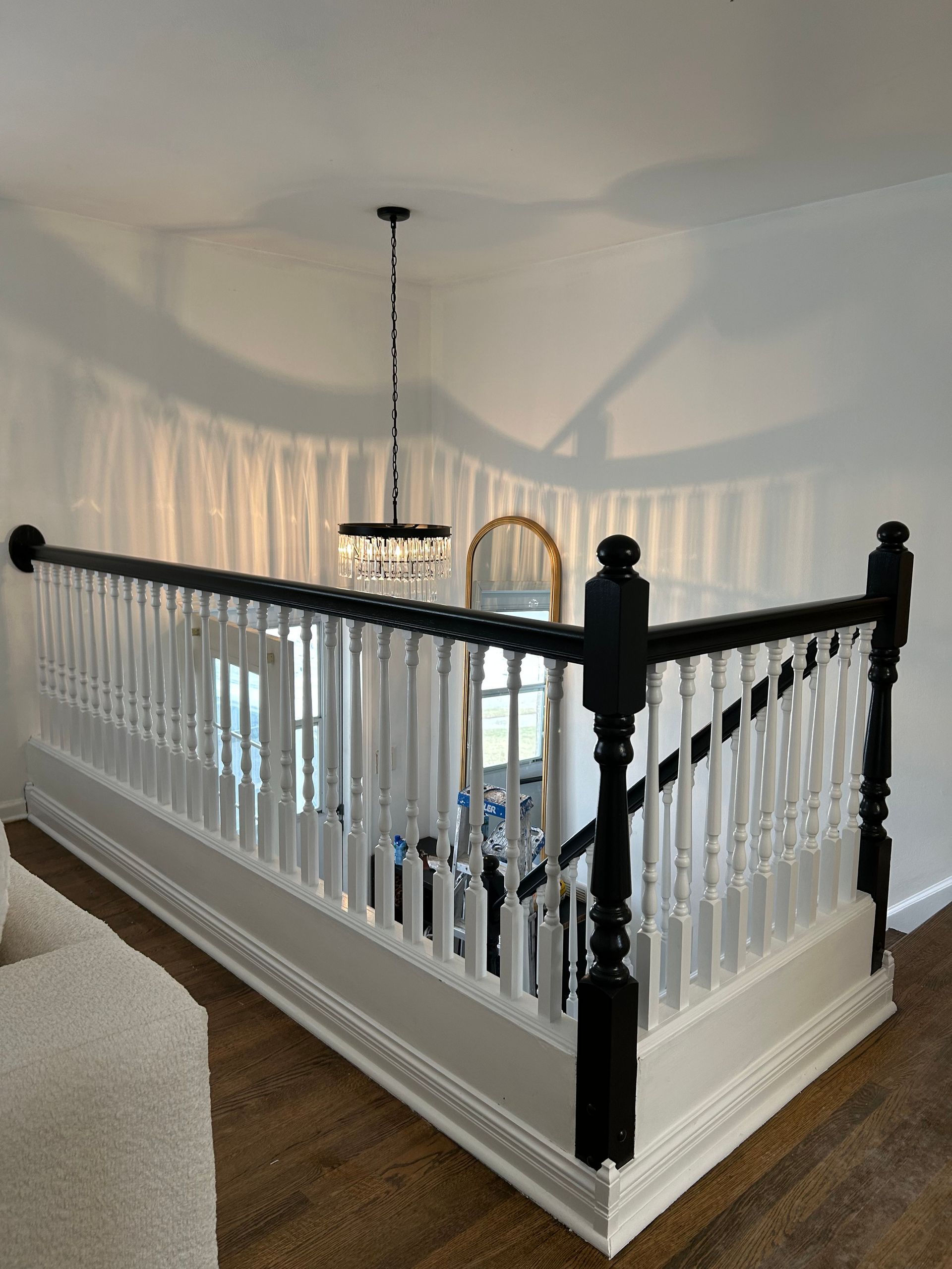 Balcony with white and black railing, chandelier, and a mirror in a light-filled room.