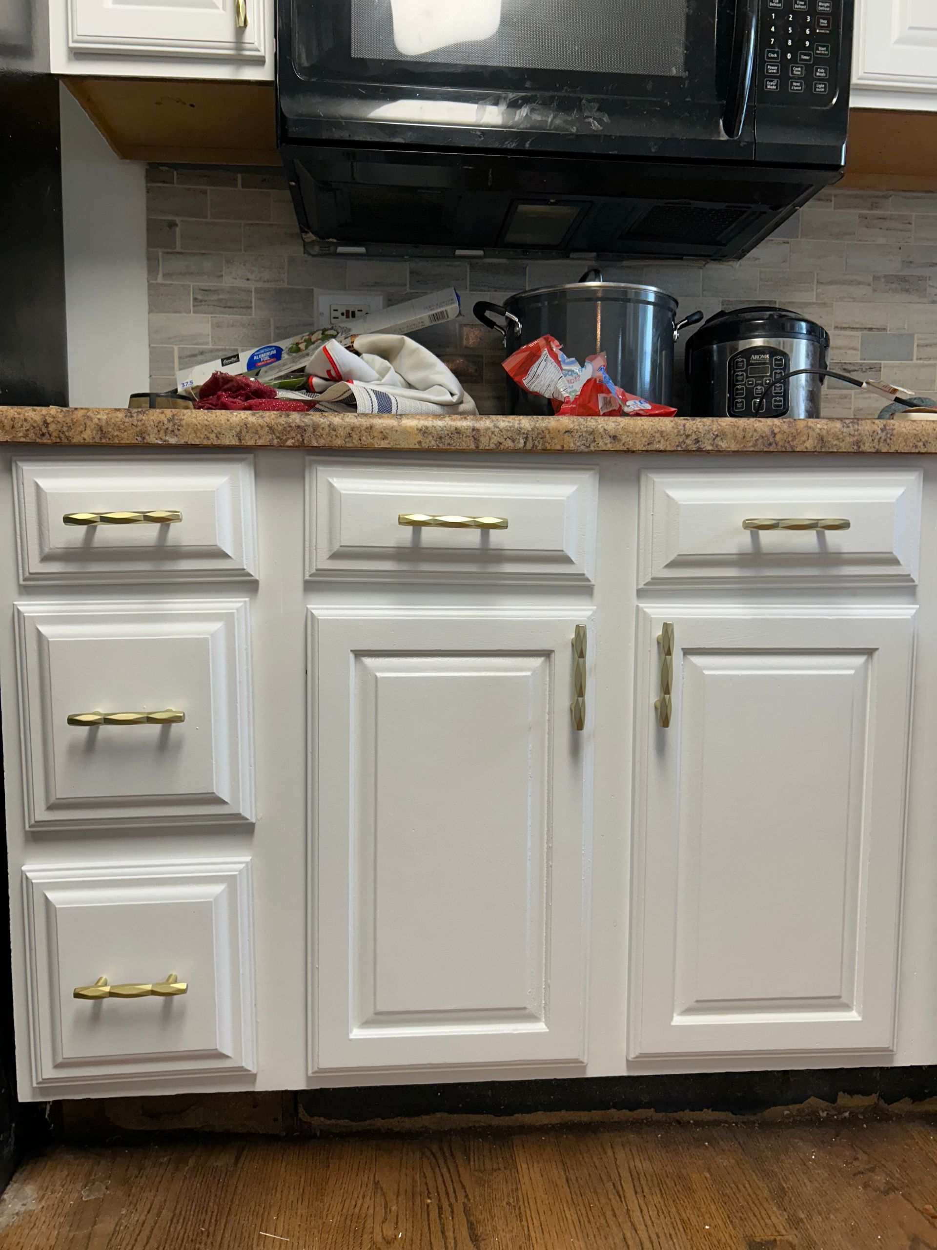 White kitchen cabinets with gold hardware beneath a microwave.