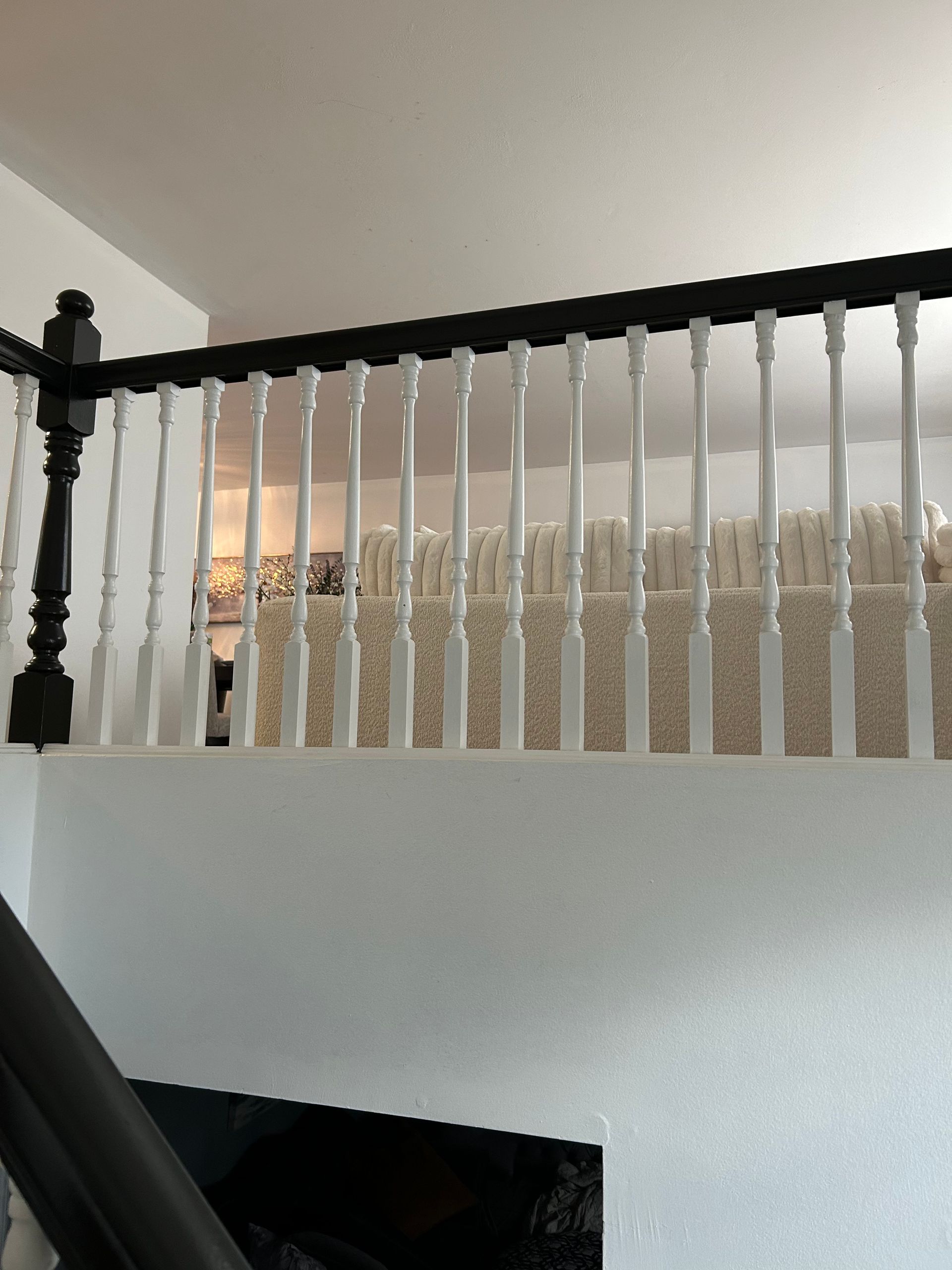 White spindles and black railing of an interior stairwell. Beige carpet visible beyond.
