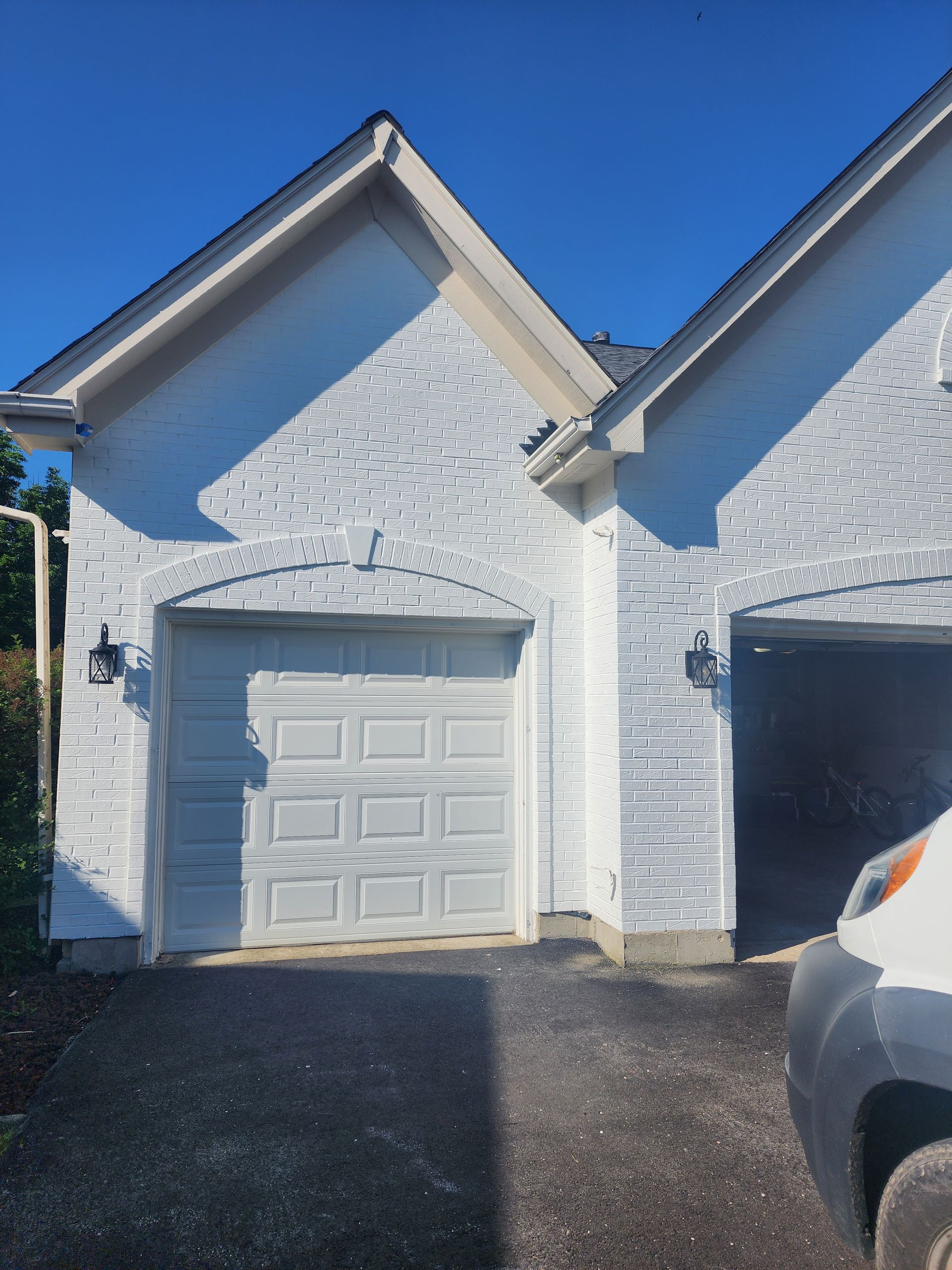 A white brick house with two garage doors and a car parked in front of it.
