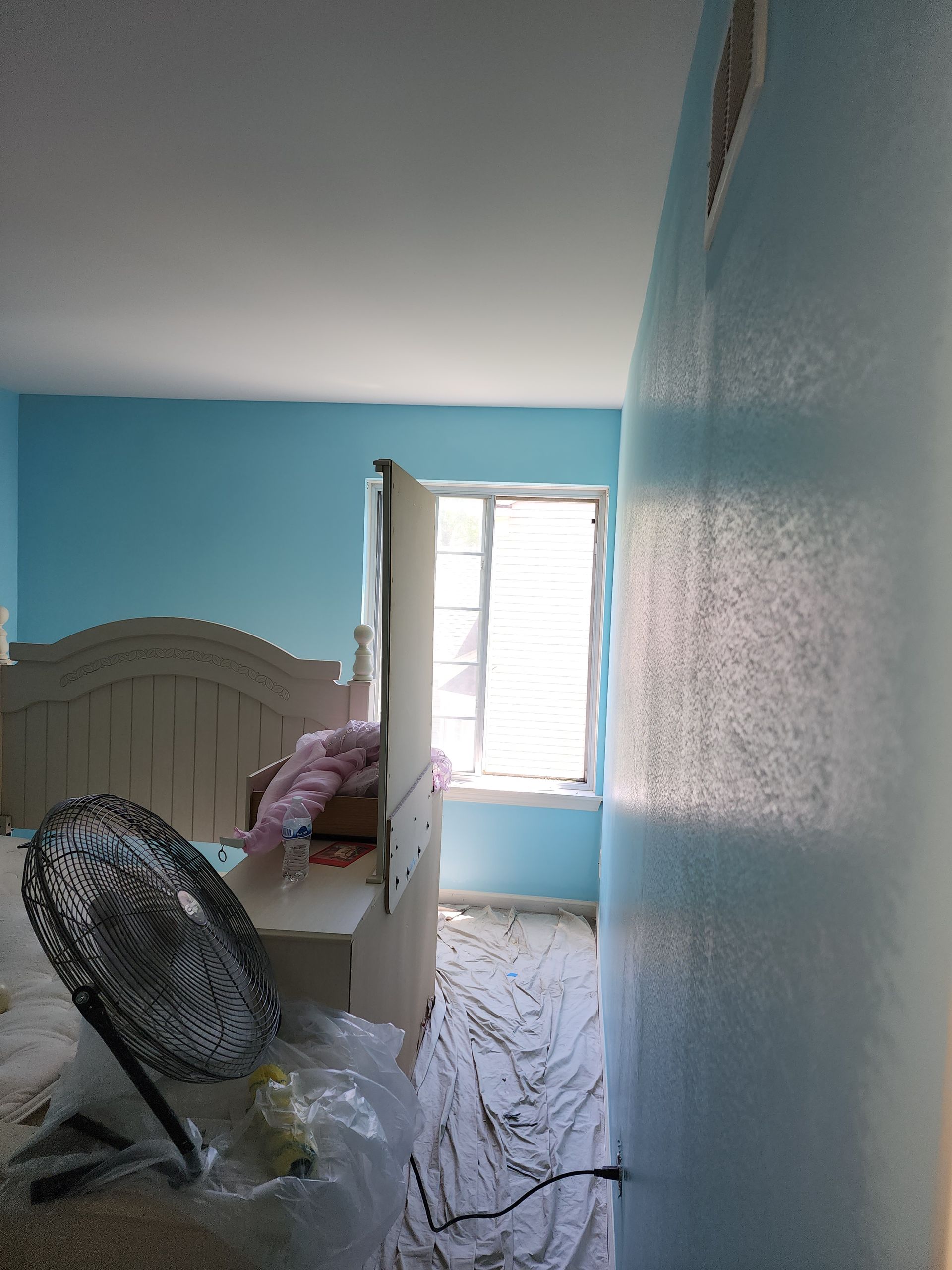 A bedroom with blue walls and a fan on the floor.