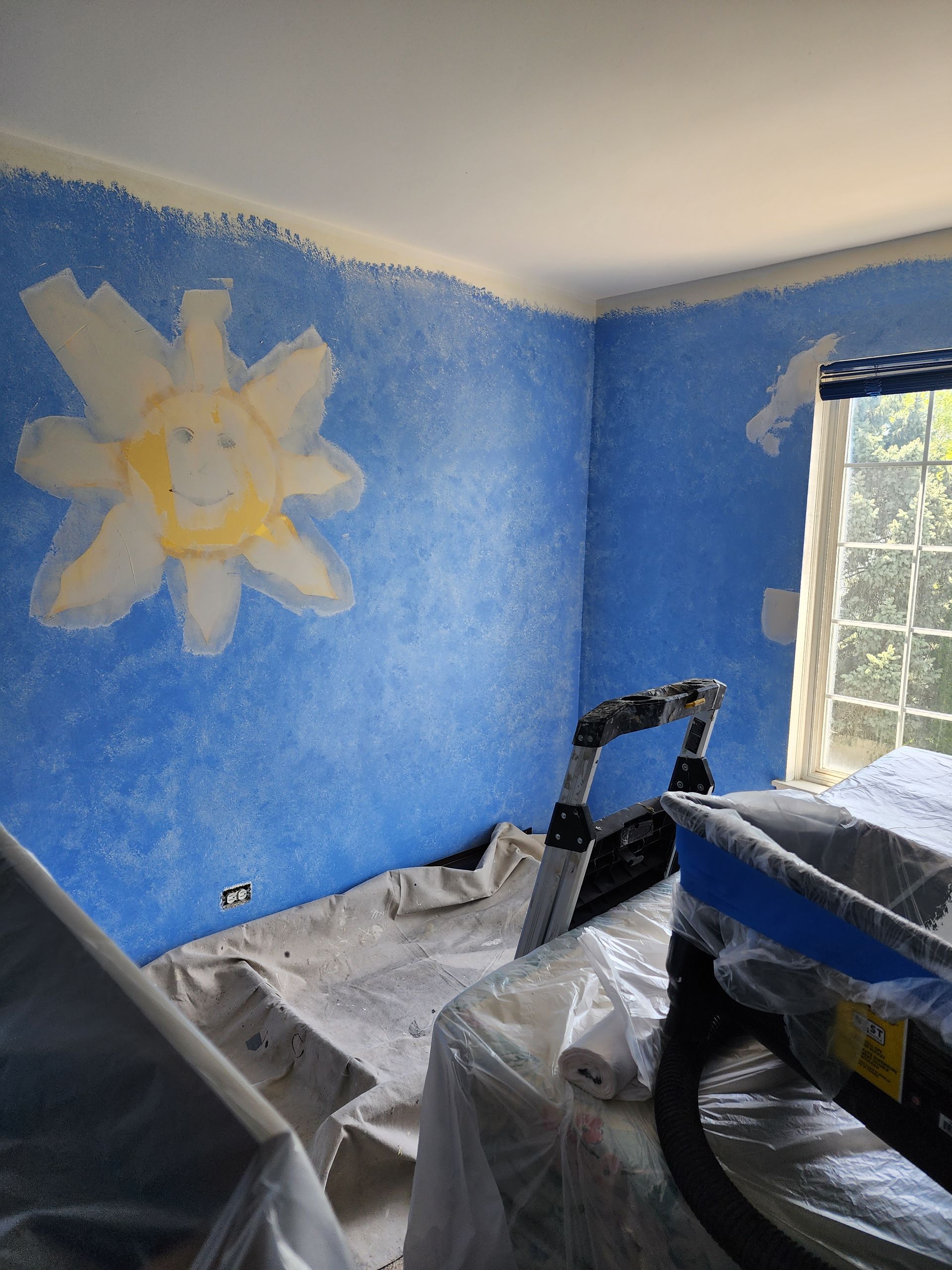 A room is being painted blue with a sun on the wall.