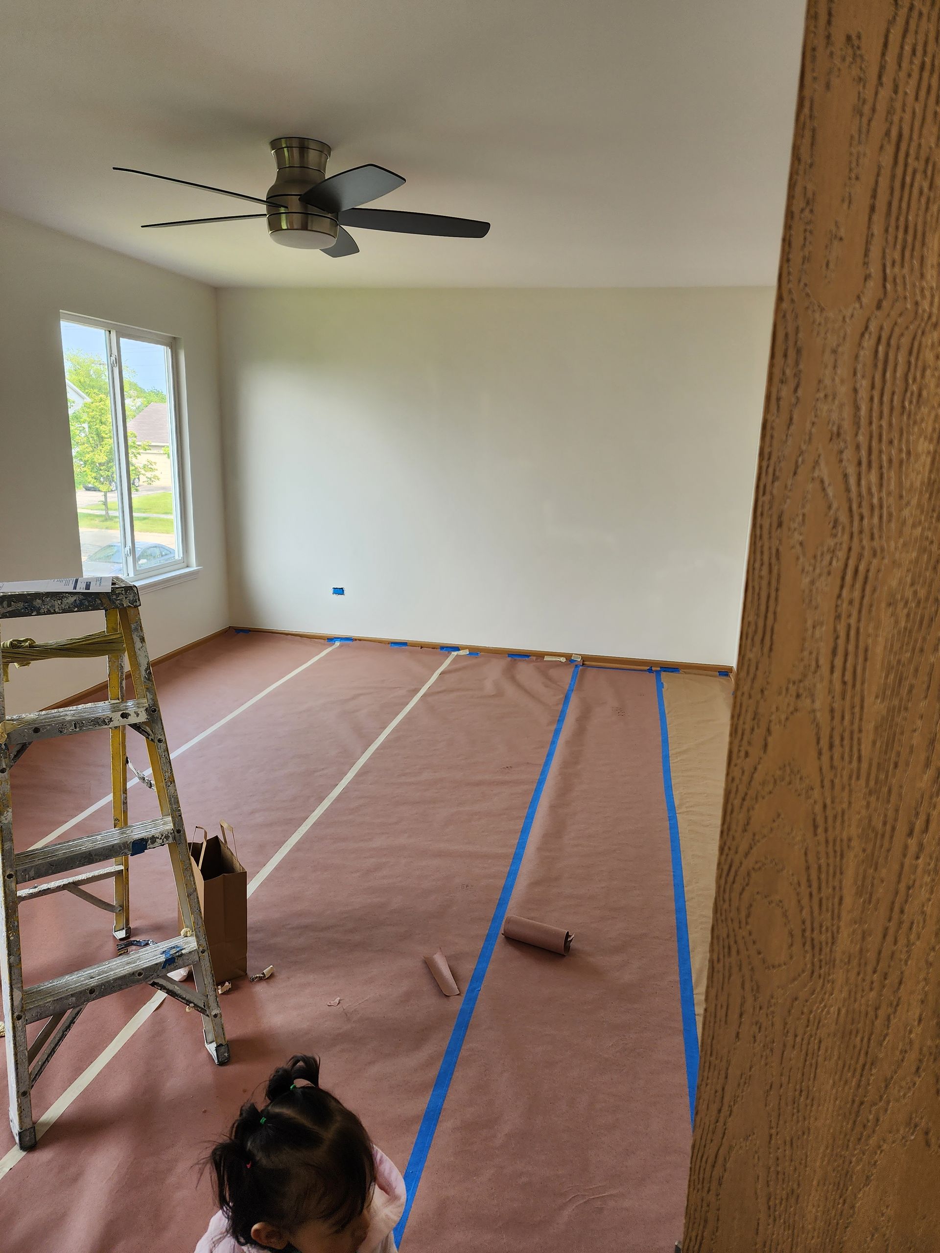 A little girl is standing in an empty room with a ceiling fan.
