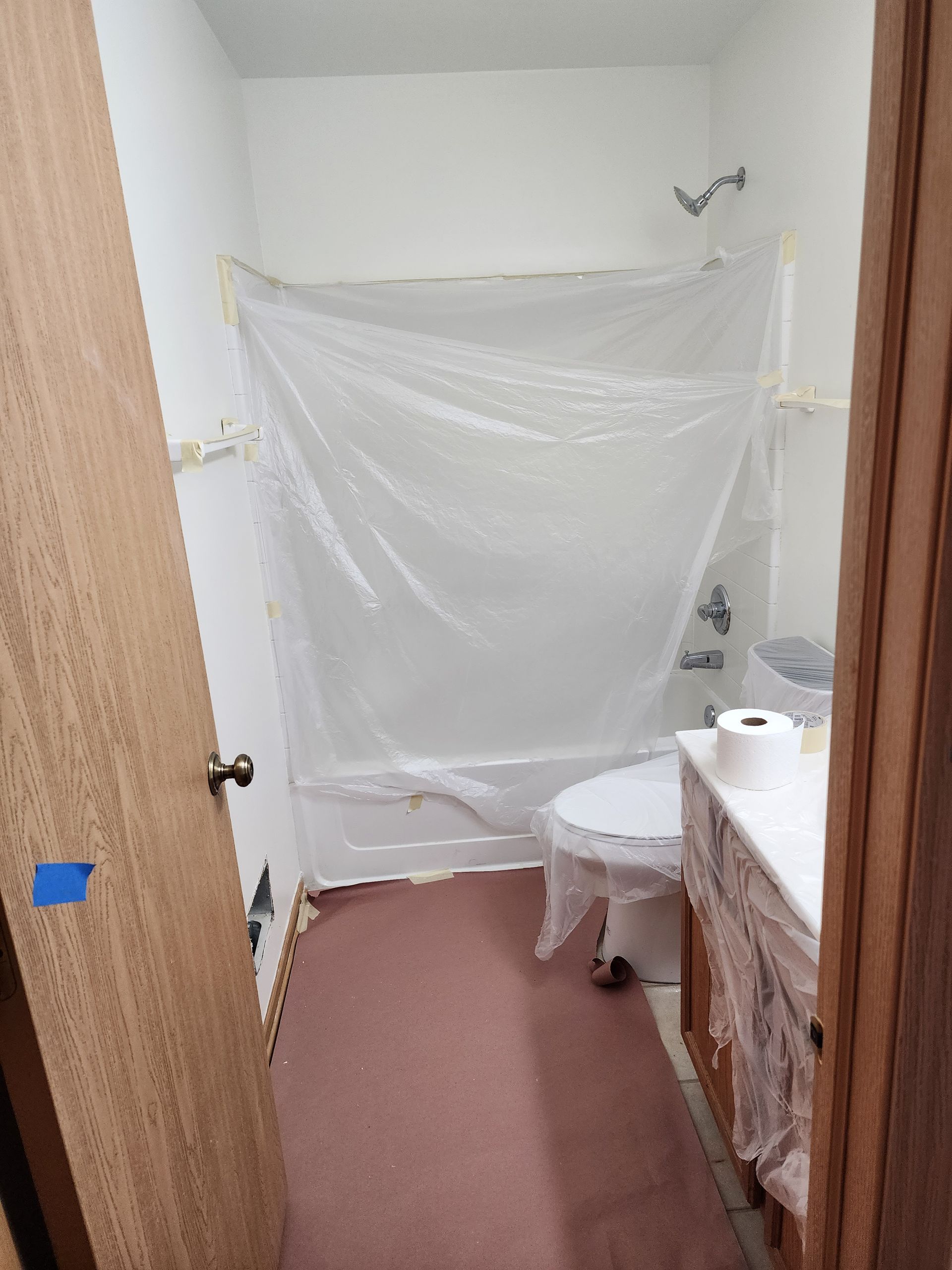 A bathroom with a toilet , tub , and shower covered in plastic.