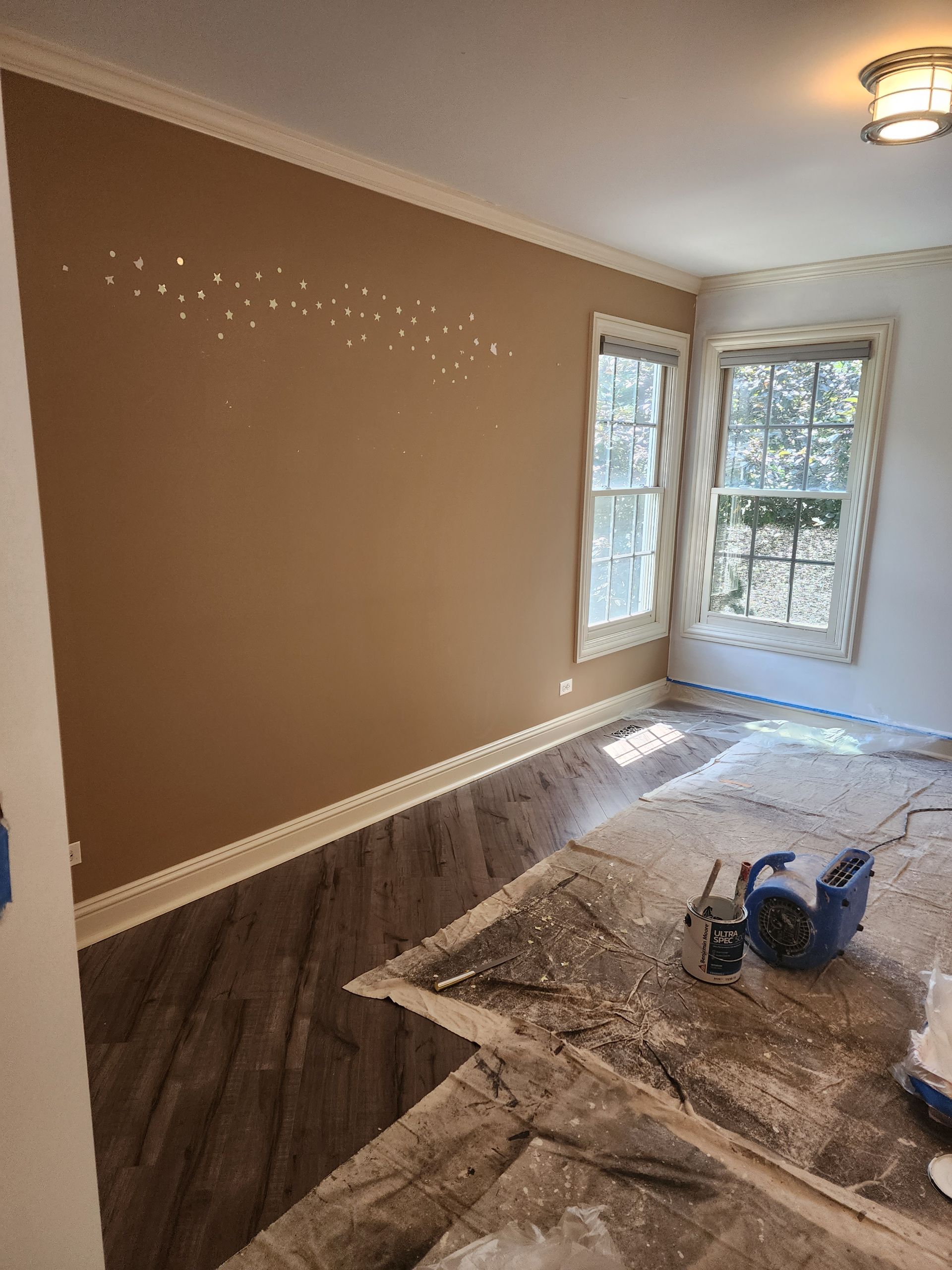 A room with brown walls and white trim is being painted.