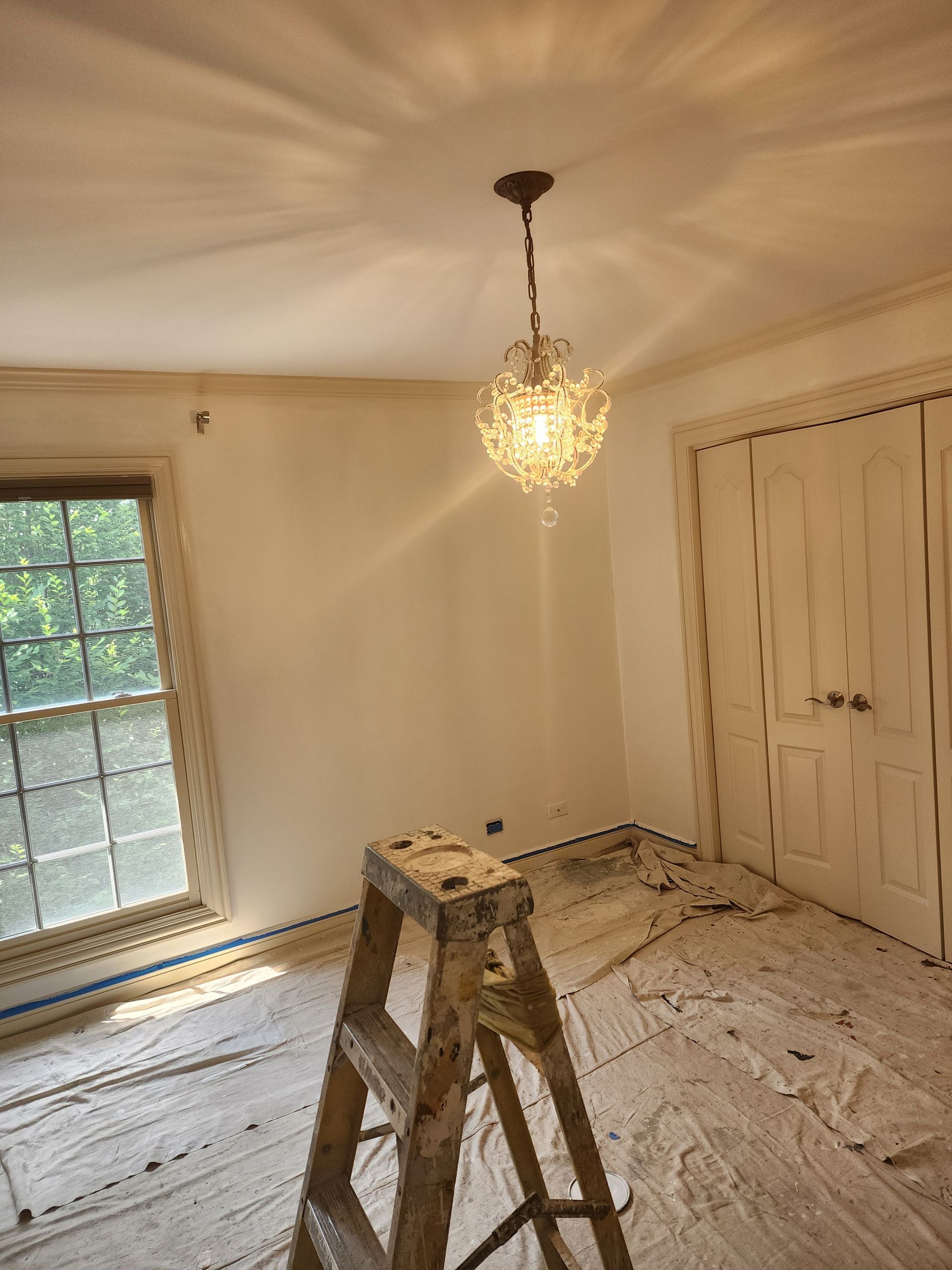 A room with a ladder and a chandelier hanging from the ceiling.