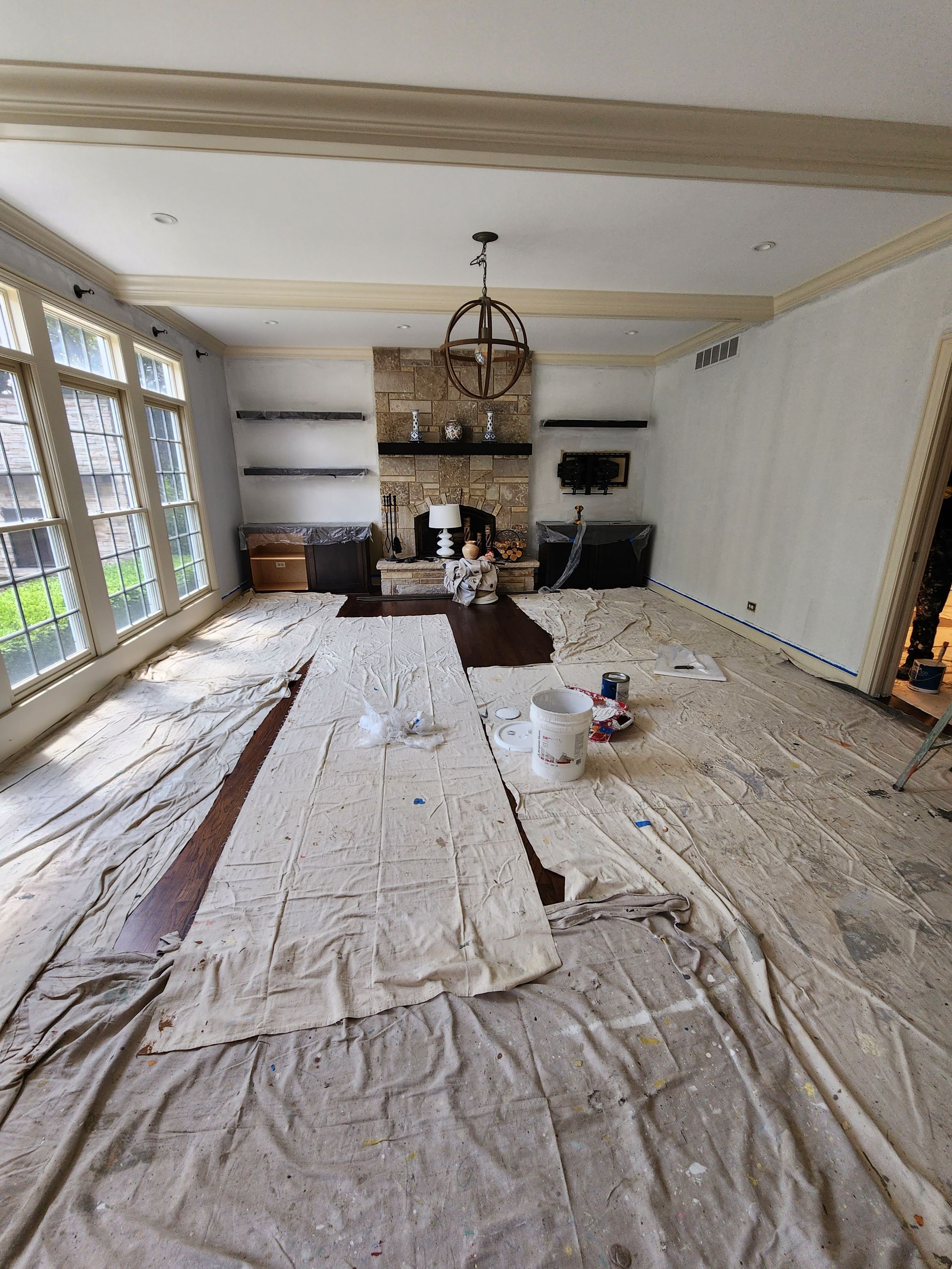A living room with a fireplace and a lot of windows is being painted.