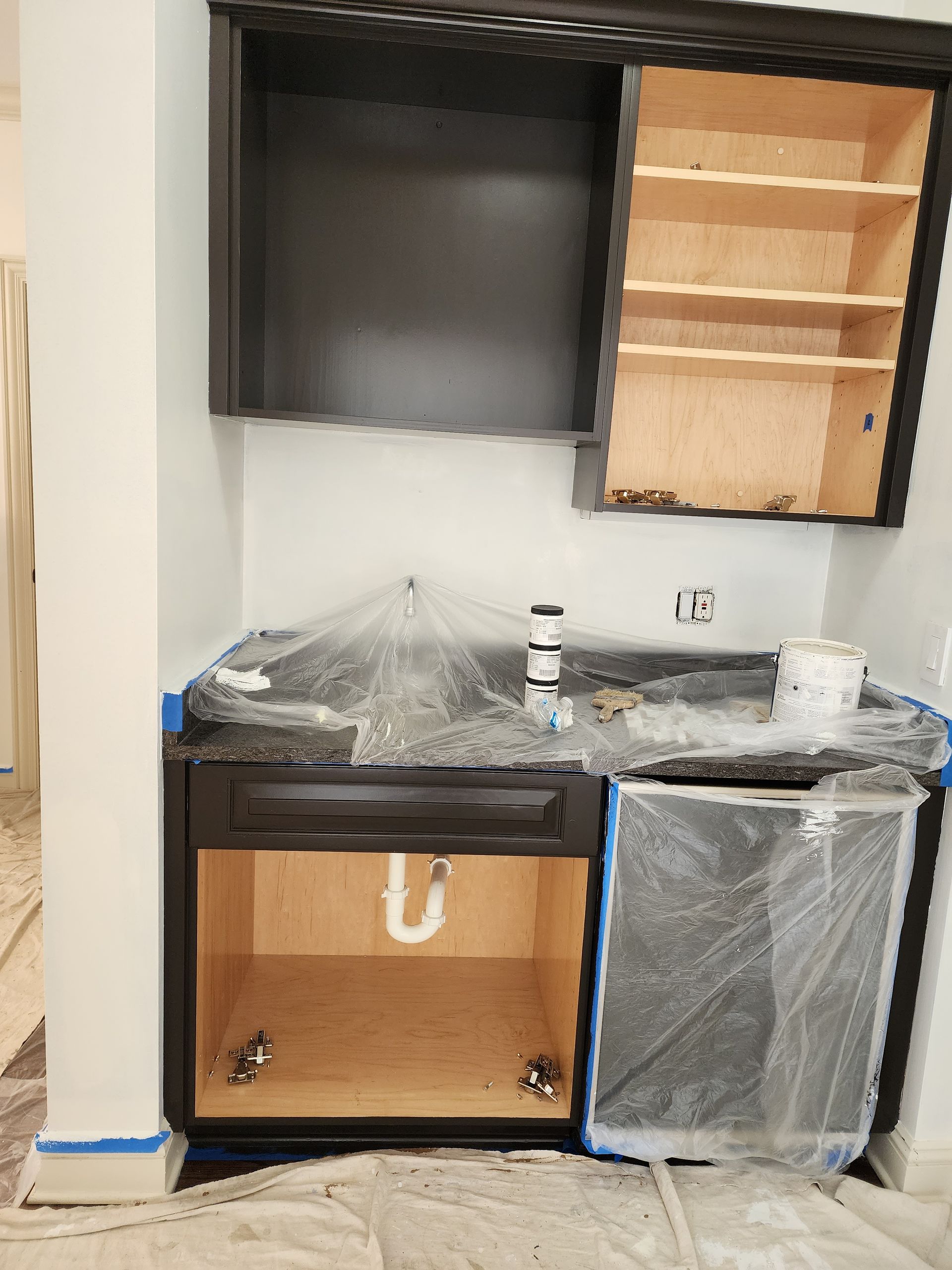A kitchen is being painted with black cabinets and a sink.