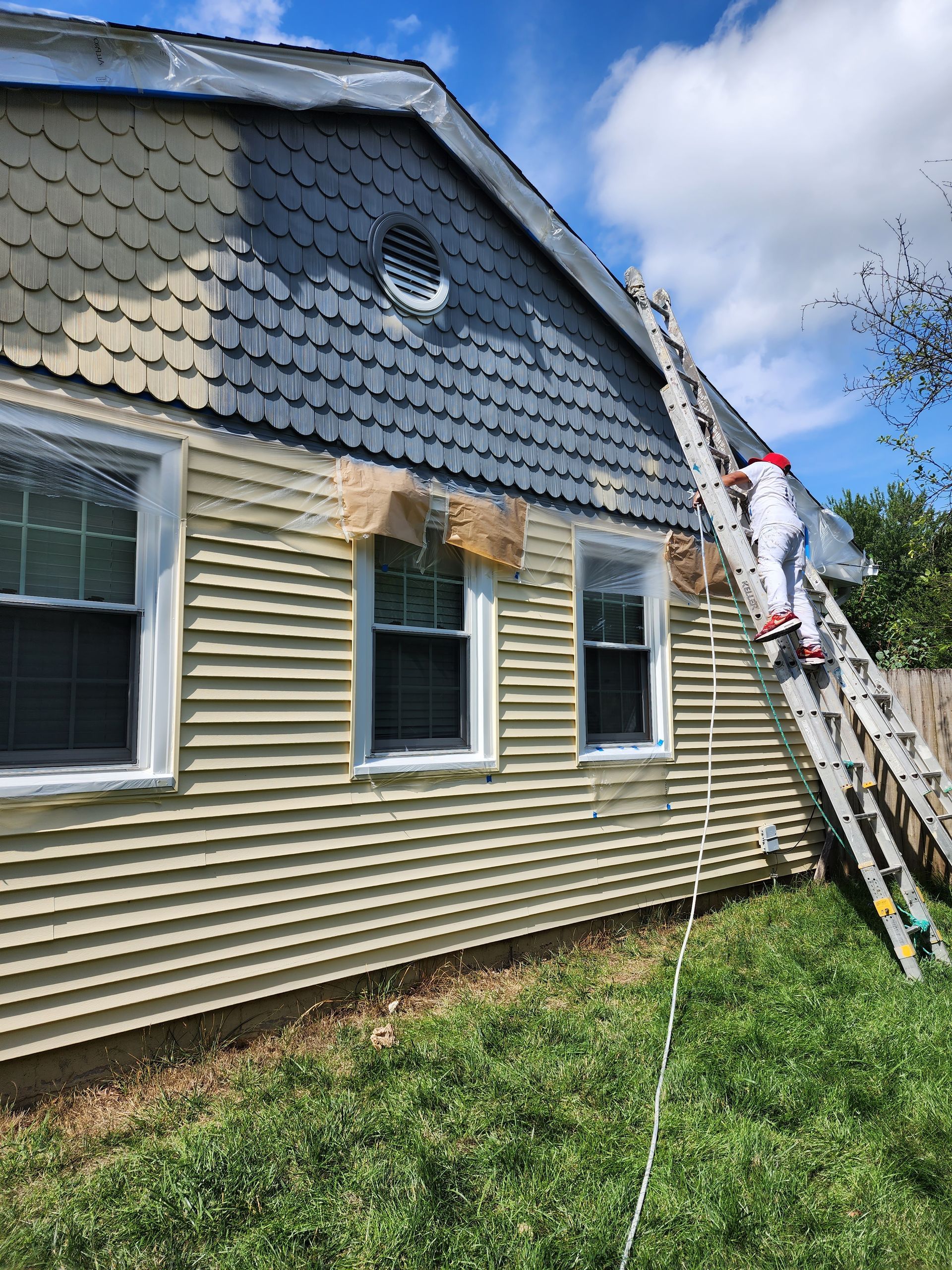 A man is painting the side of a house with a ladder.
