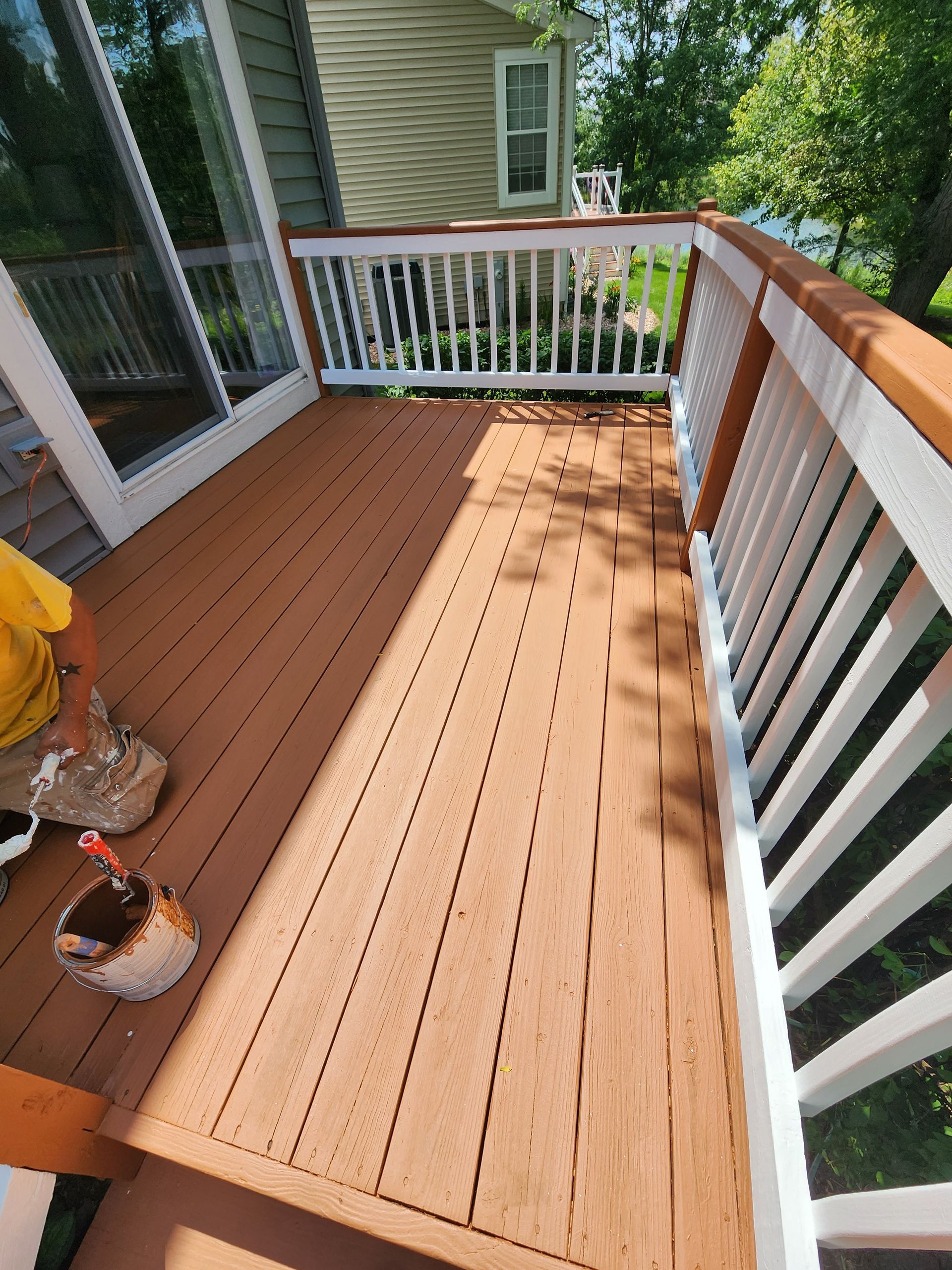 A man is painting a wooden deck with a white railing.