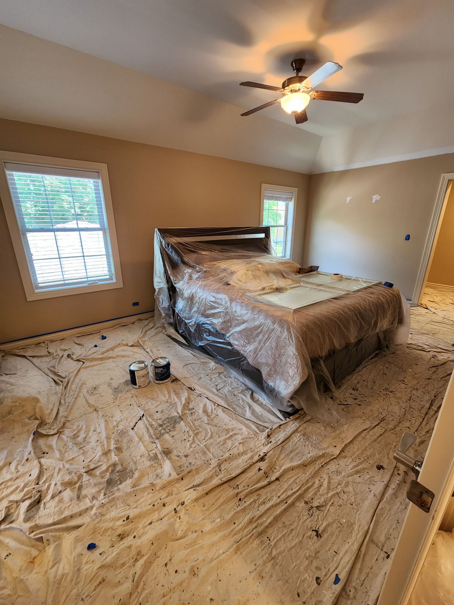 A bedroom with a bed covered in plastic and a ceiling fan.