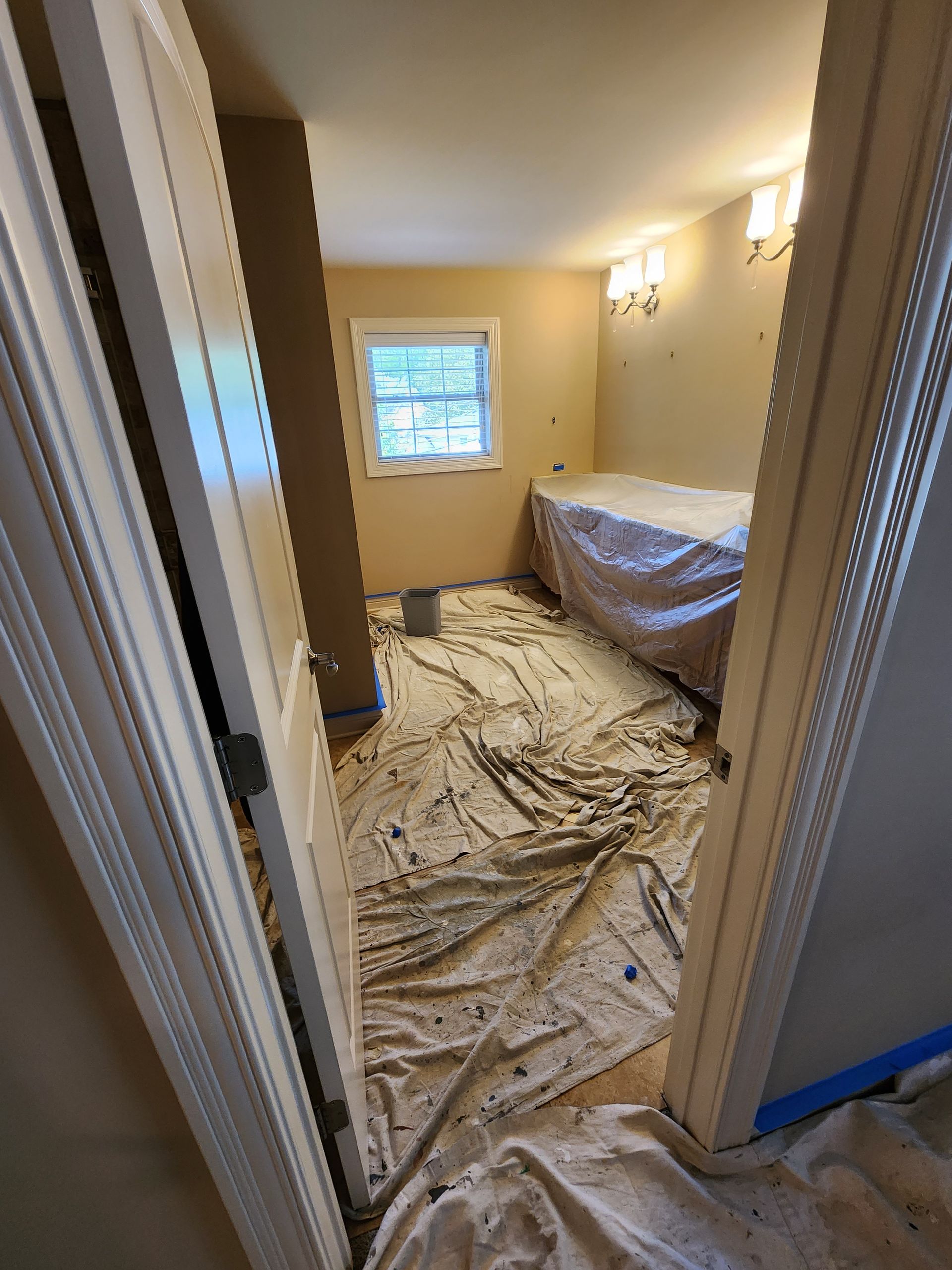 A room with a bed and a window is being painted.
