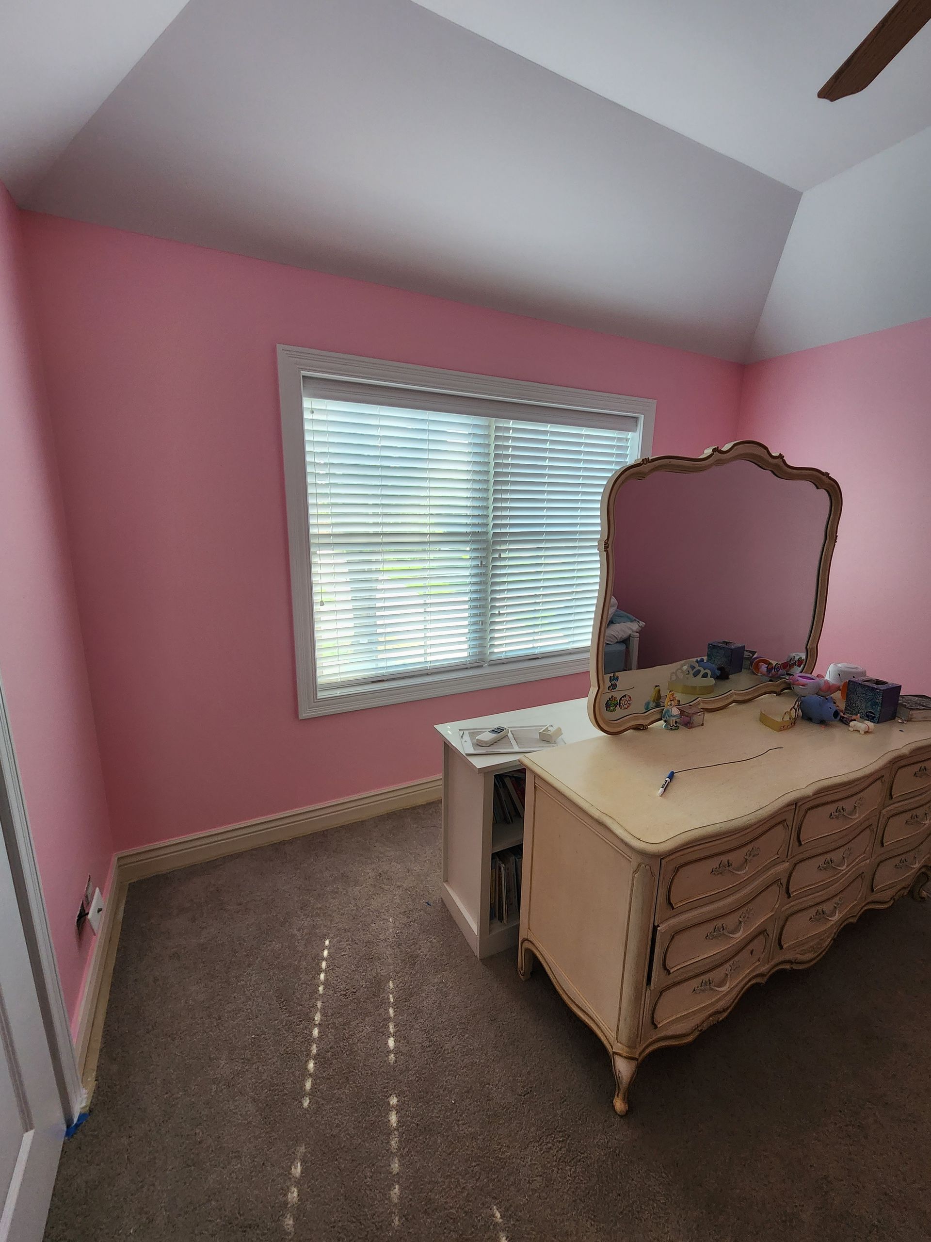 A bedroom with pink walls and a dresser and mirror