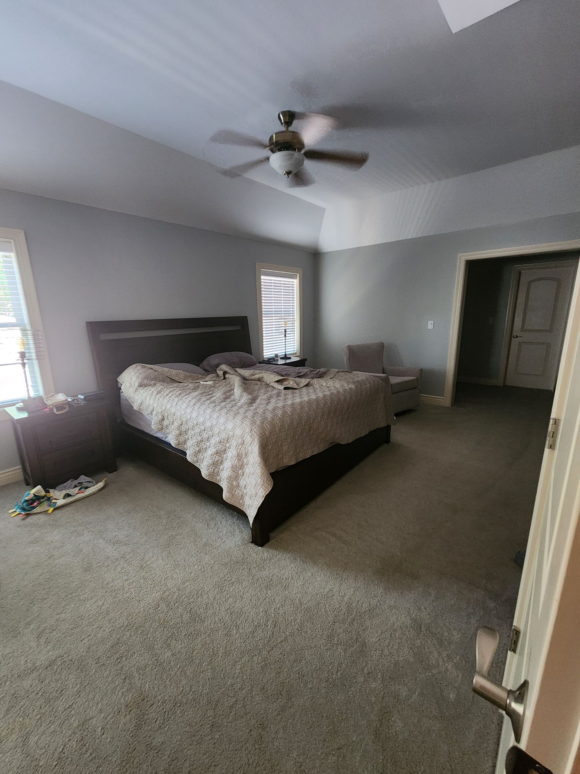 A bedroom with a bed , nightstand , chair and ceiling fan.
