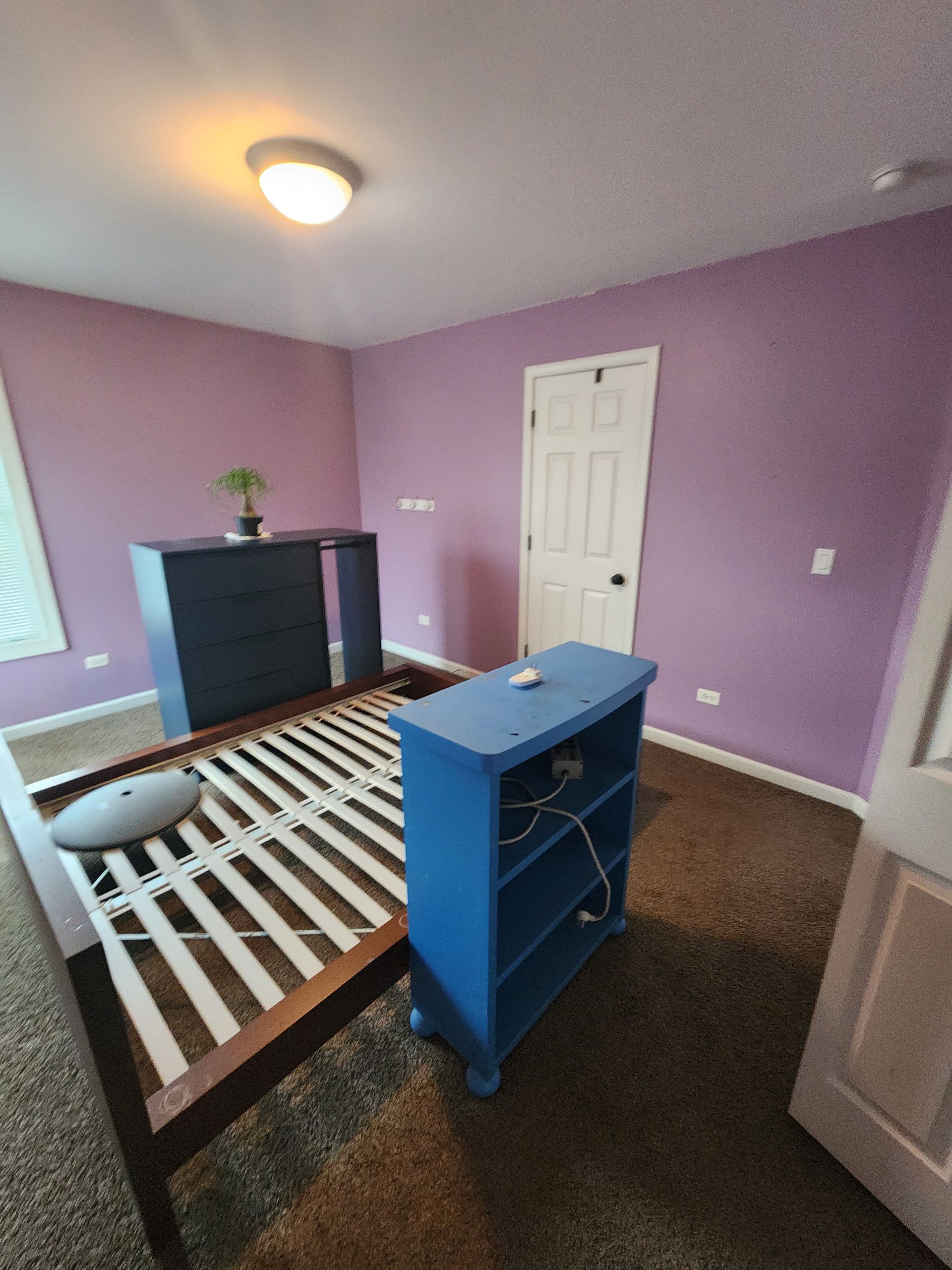 A bedroom with purple walls and a blue shelf in the middle of the room.