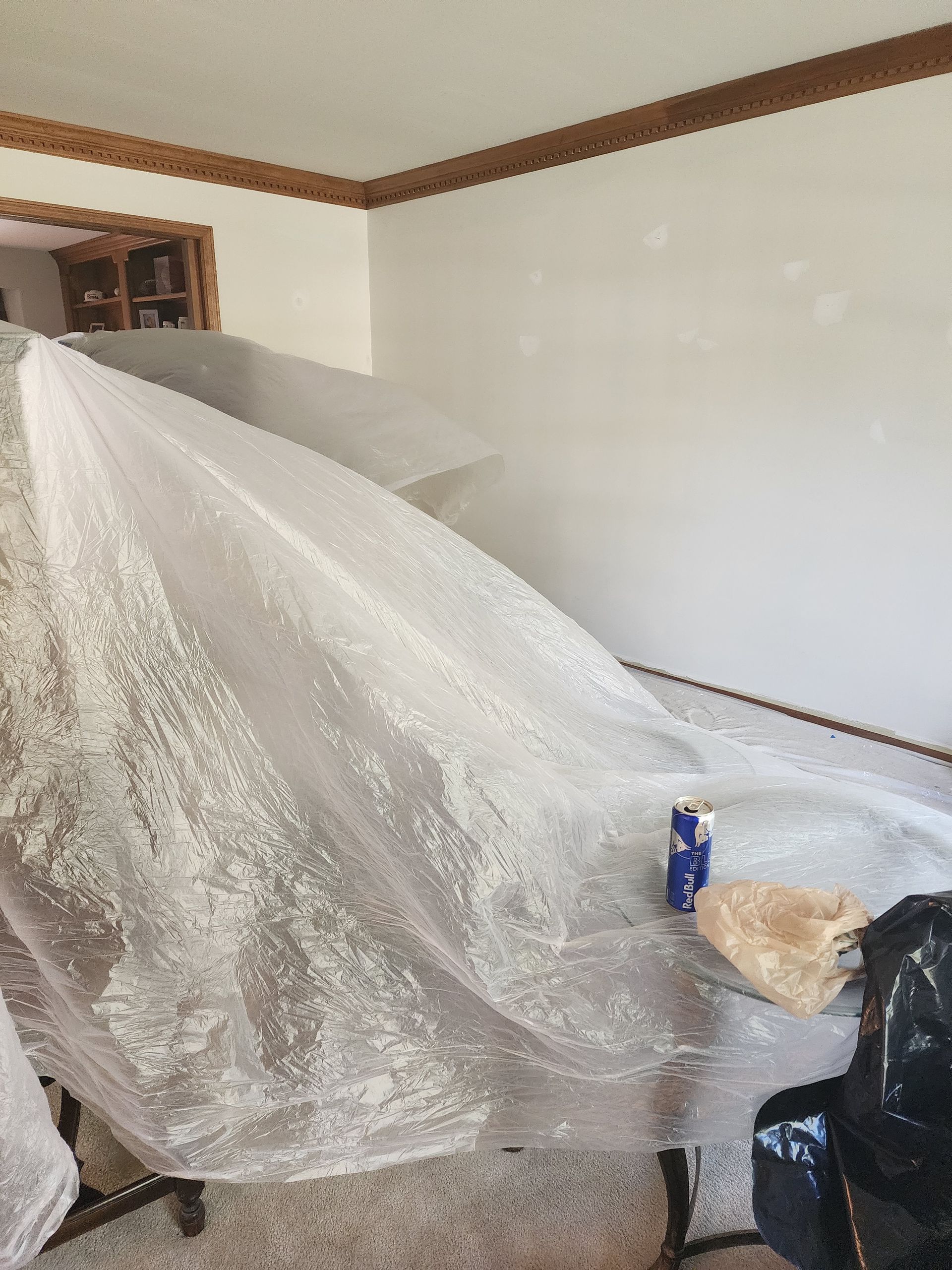 A wedding dress is covered in plastic wrap in a living room.