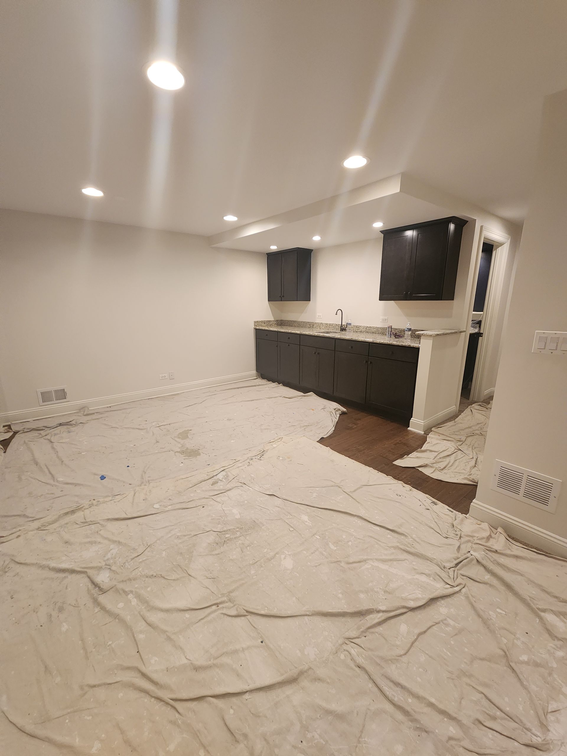 A room with a lot of white sheets on the floor and a kitchen in the background.