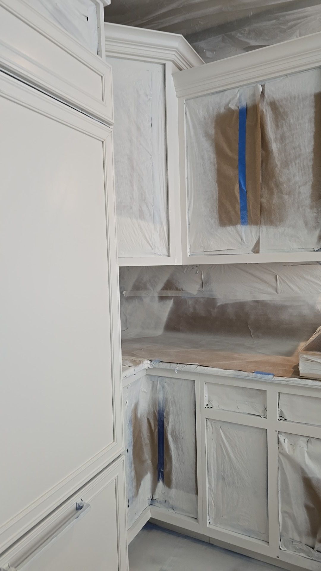 A kitchen is being painted white and covered in plastic.