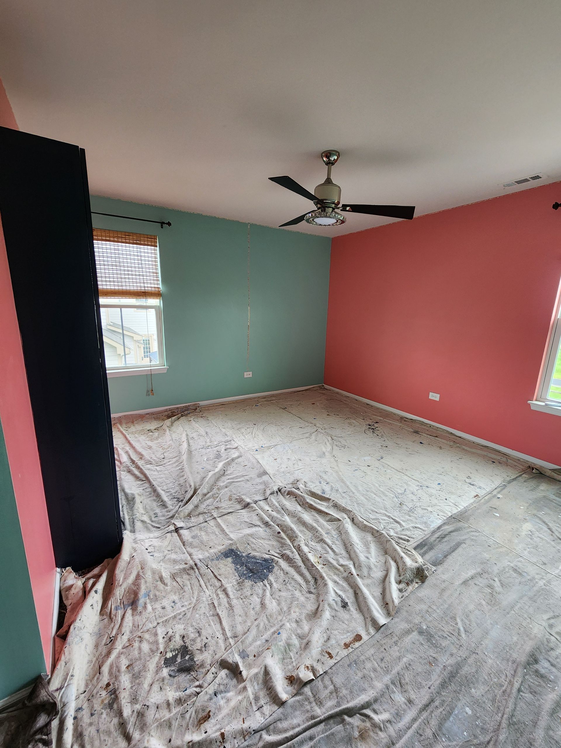 An empty room with pink and green walls and a ceiling fan.