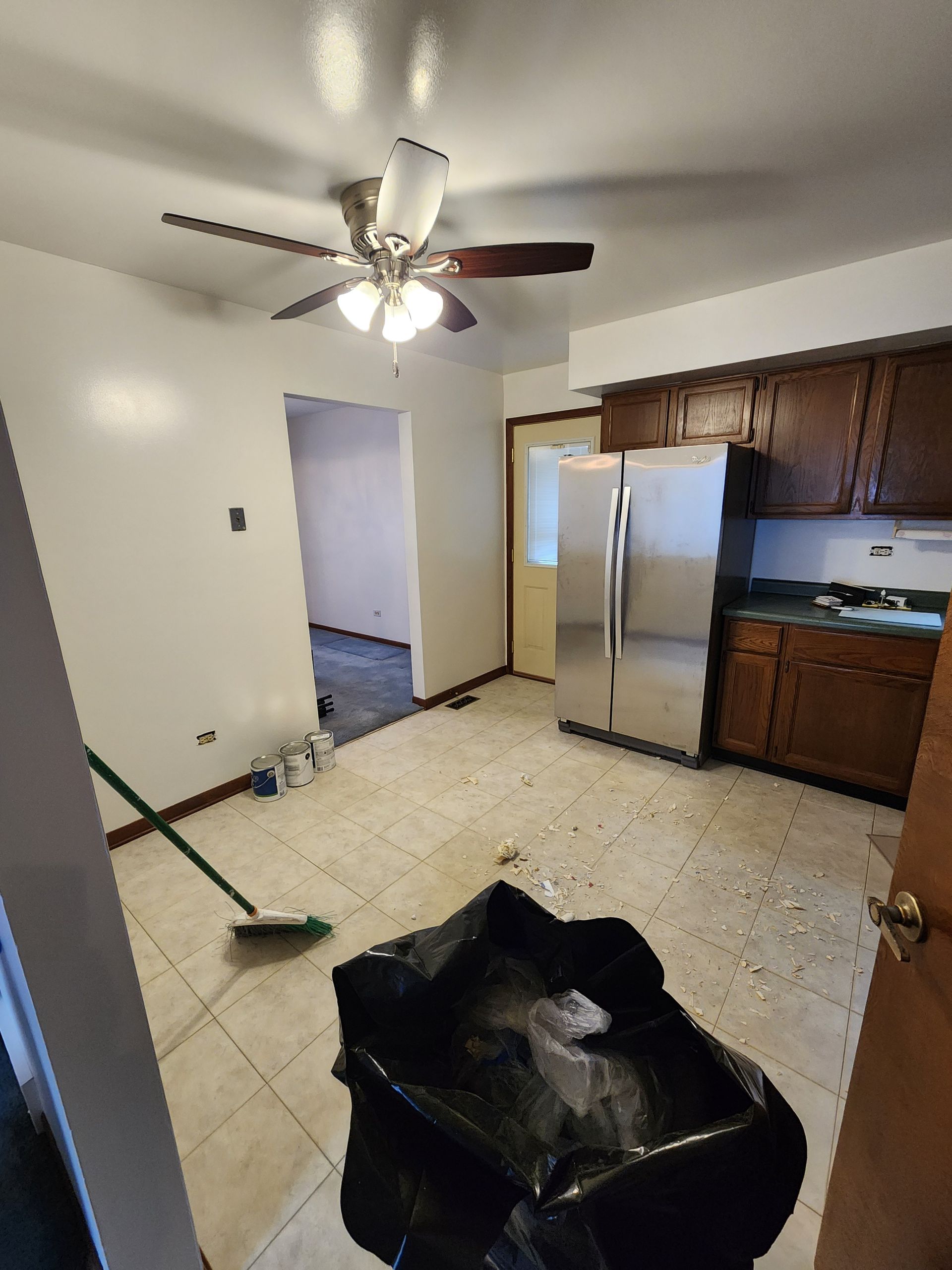 A kitchen with a ceiling fan and a trash bag on the floor.
