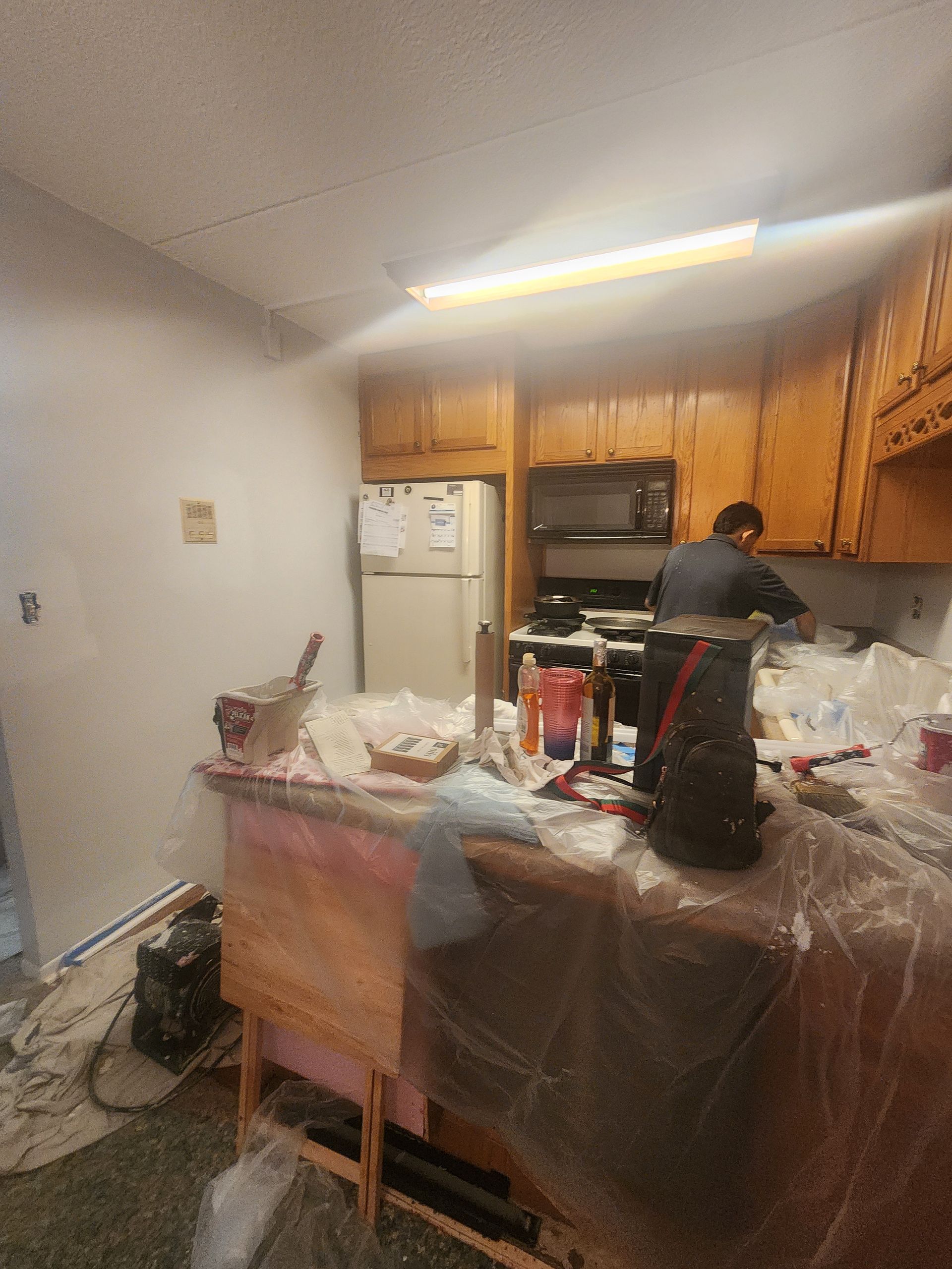 A man is painting a kitchen with wooden cabinets and a refrigerator.