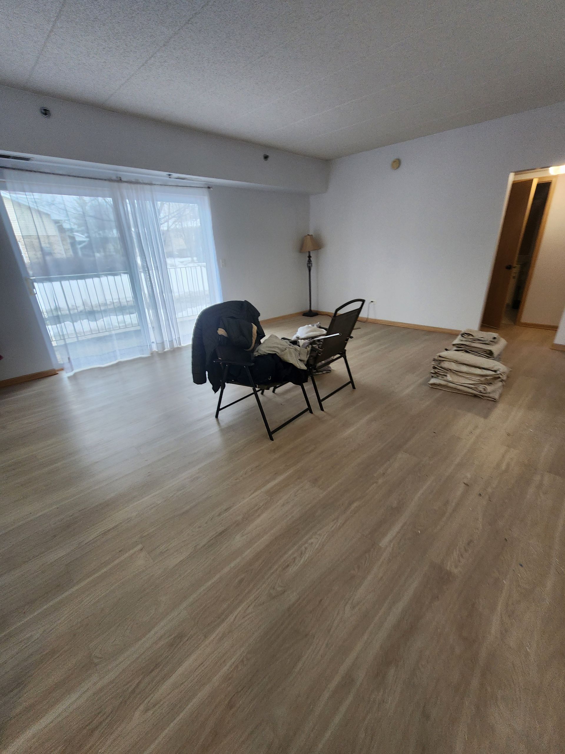 A living room with a wooden floor , chairs and a table.
