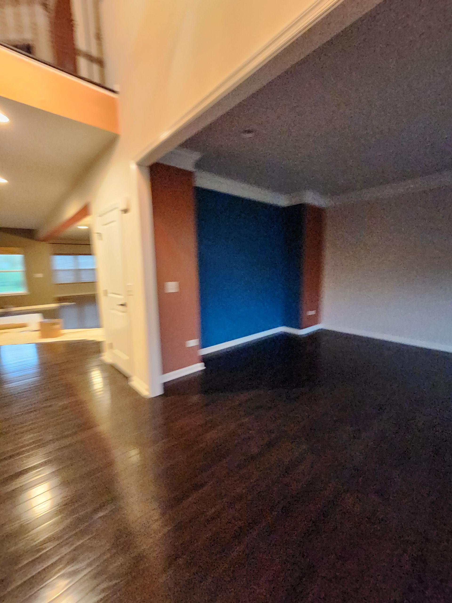 An empty living room with hardwood floors and a blue wall.