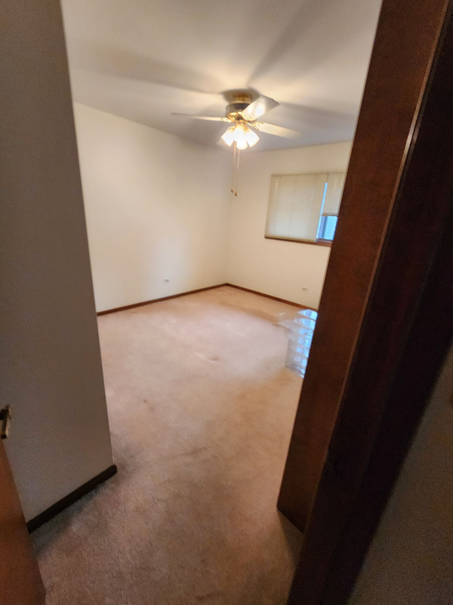 An empty bedroom with a ceiling fan and a window.