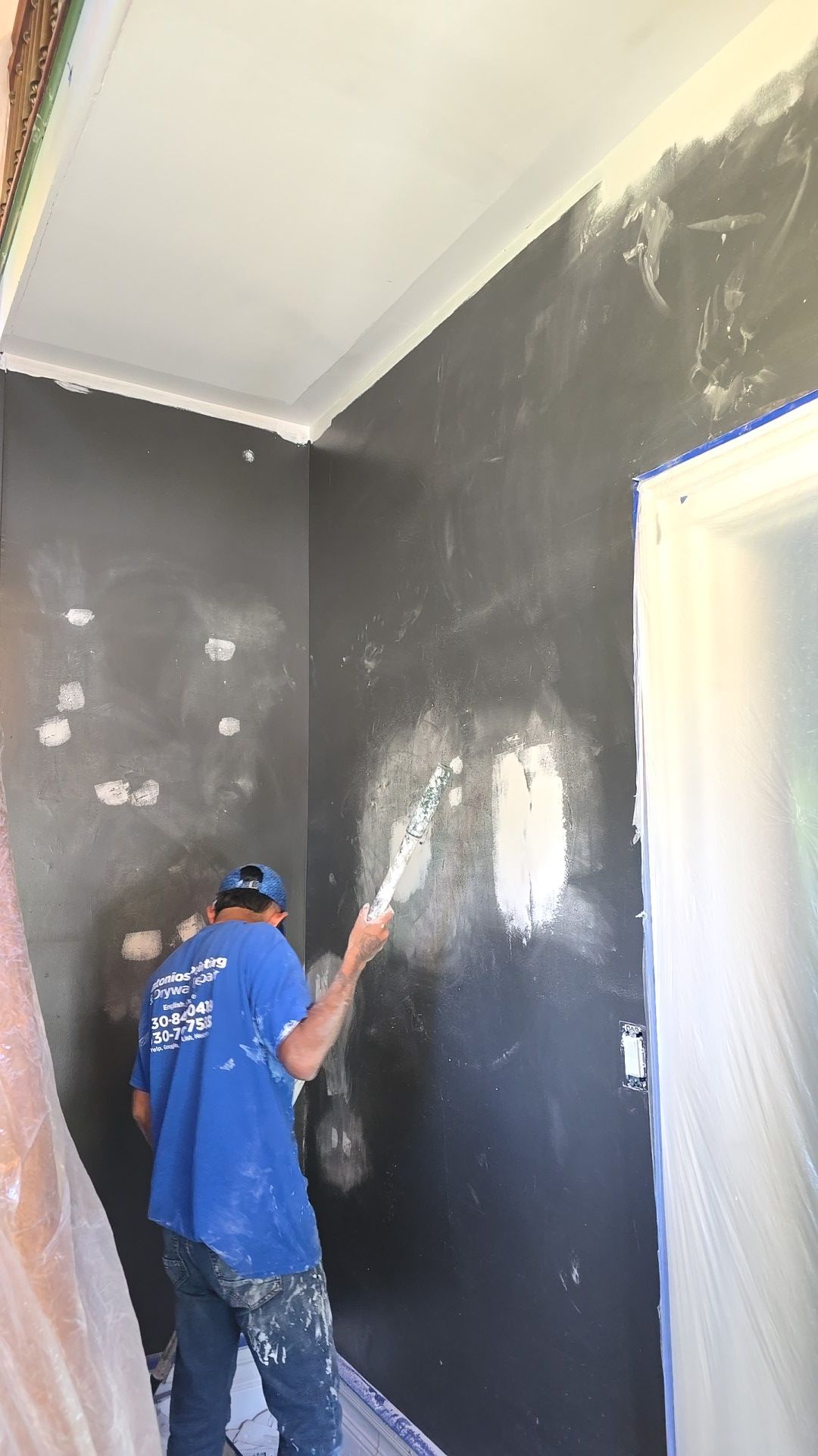 A man in a blue shirt is painting a wall.