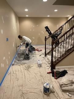 A man is painting a wall in a basement next to a staircase.