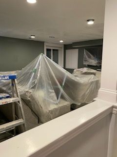 A room with a ladder and a couch covered in plastic.