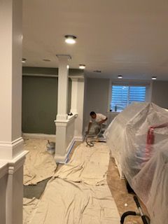 A man is painting a room in a basement with a vacuum cleaner.