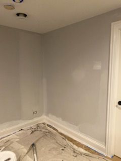A room with gray walls and white trim is being painted.