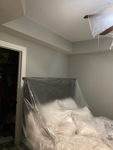 A bed is covered in plastic in a room with a ceiling fan.