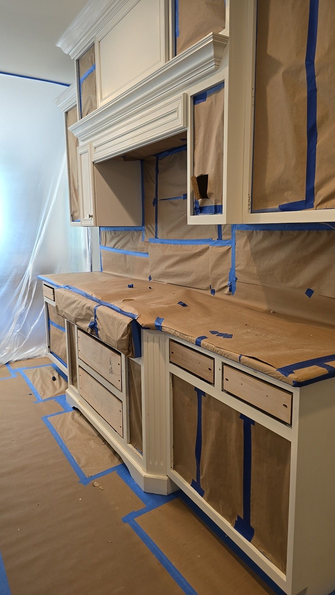 A kitchen is being painted with blue tape and paper towels.
