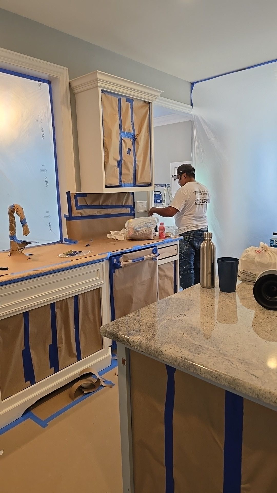 A man is painting a kitchen with blue tape.