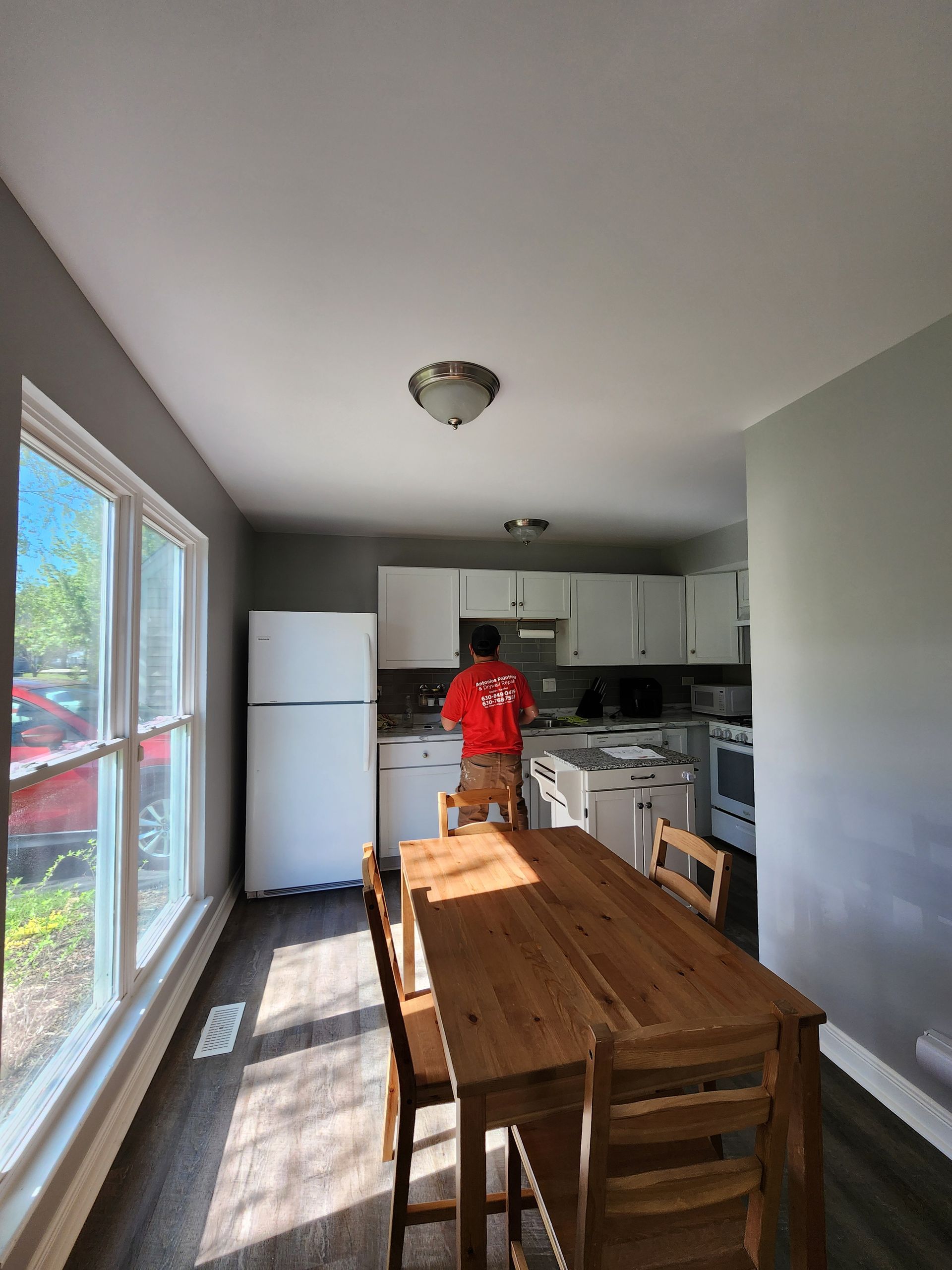 A man in a red shirt is standing in a kitchen with a table and chairs.