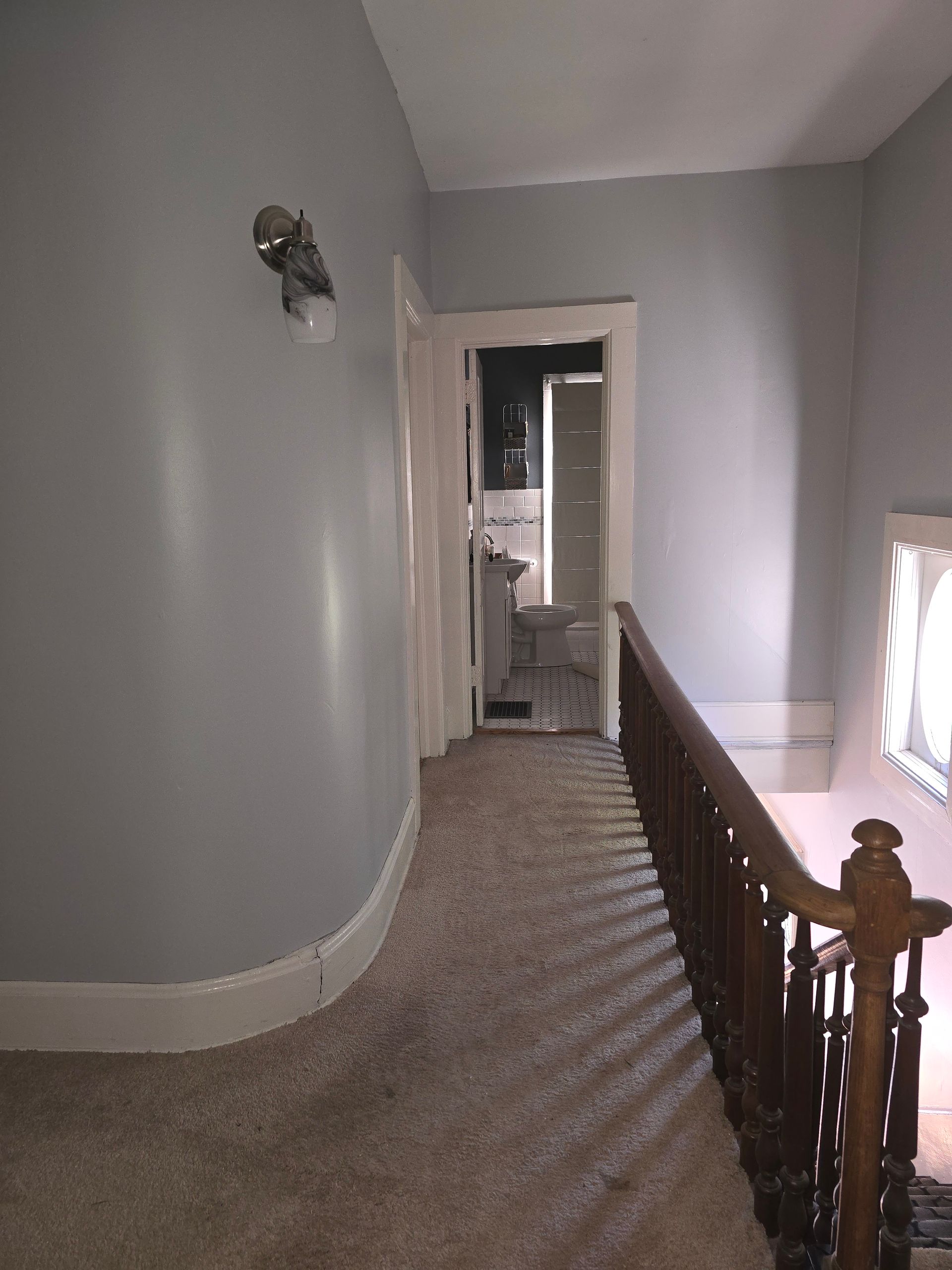 A hallway with a wooden railing leading to a bathroom.