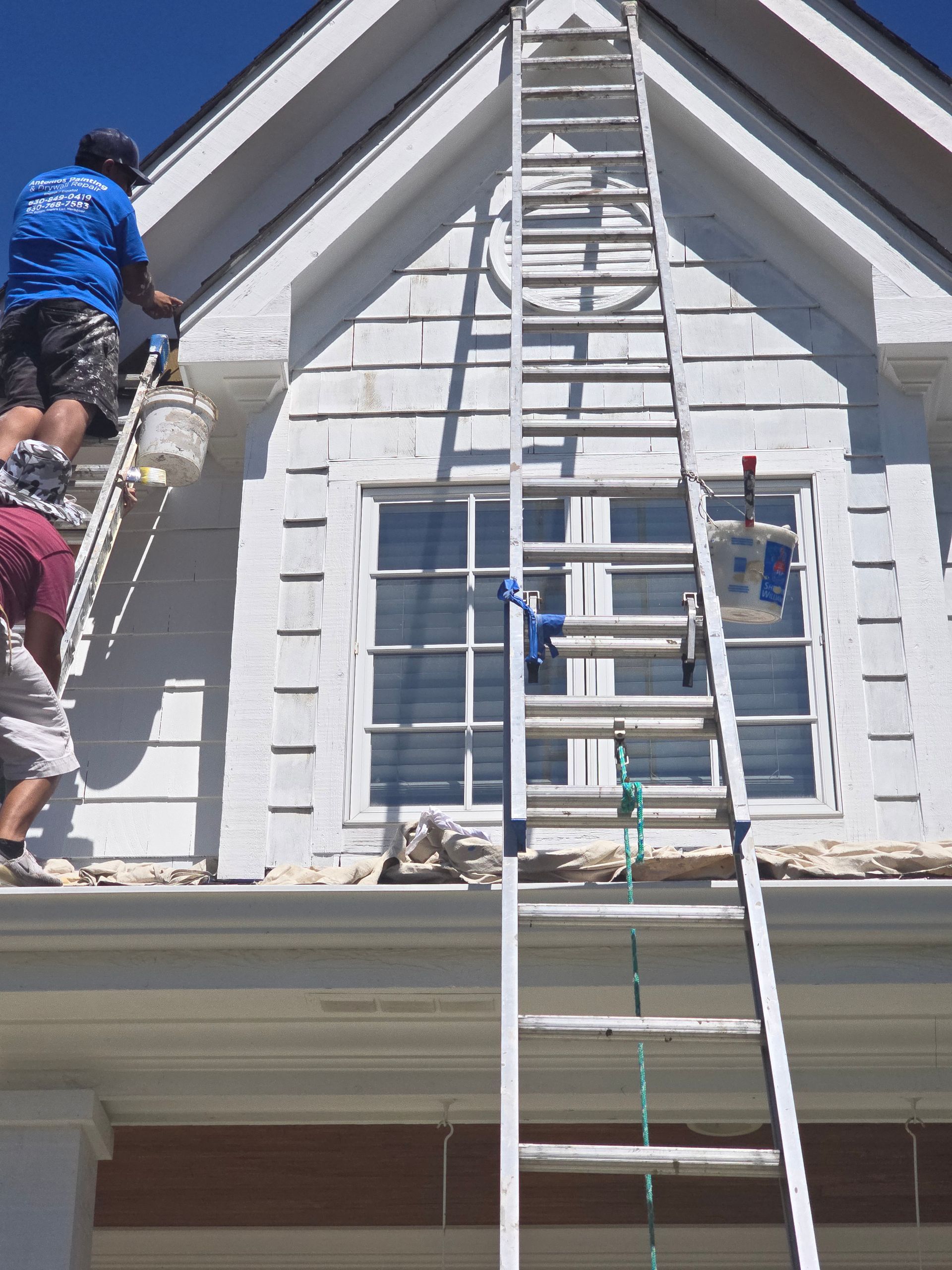 A man on a ladder paints the side of a house