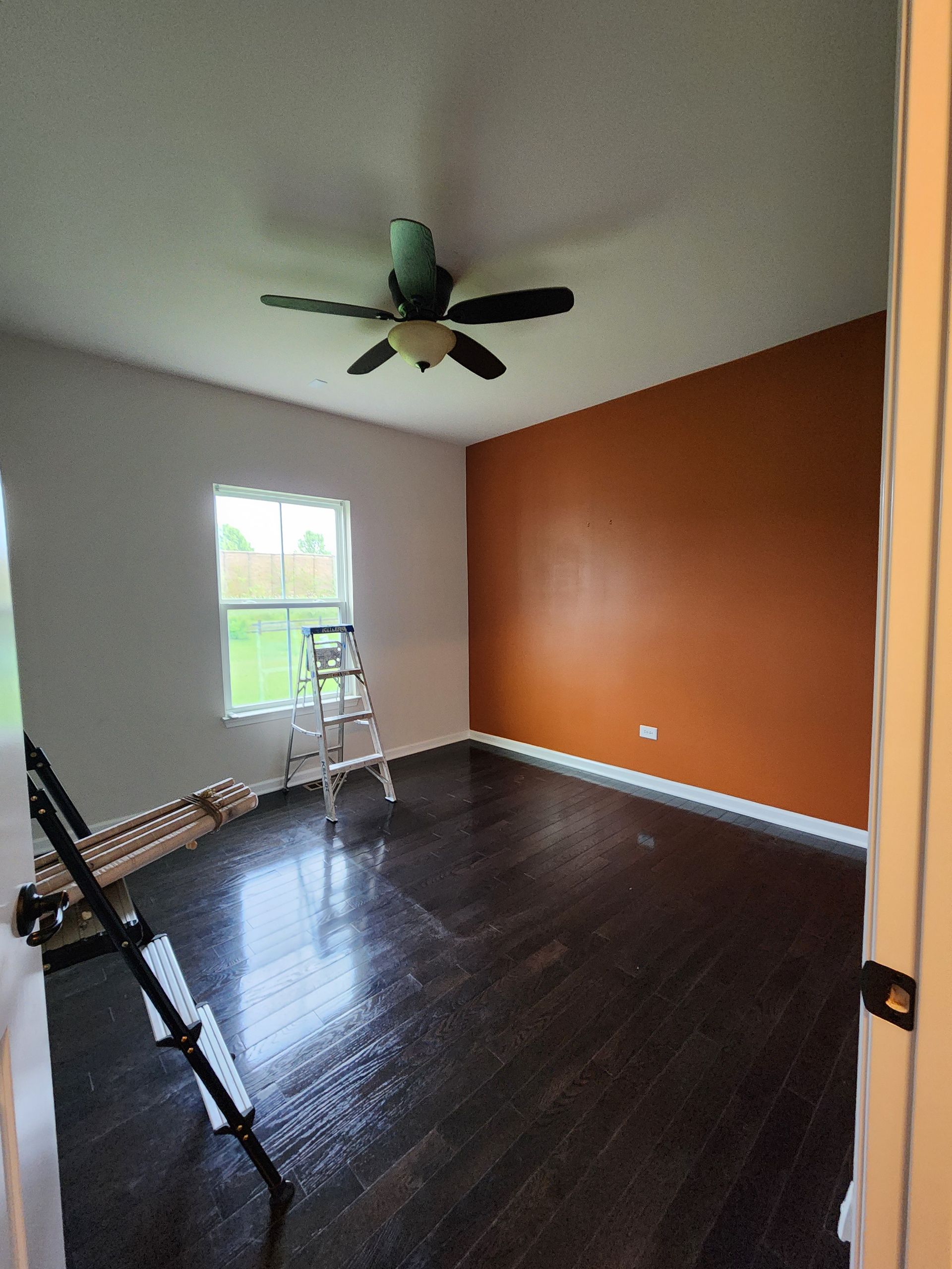 A room with a ceiling fan and a ladder in it.