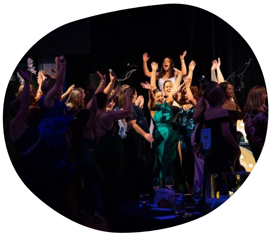 Audience cheering at a band on stage, singer in green gown, arms raised in celebration, black background.