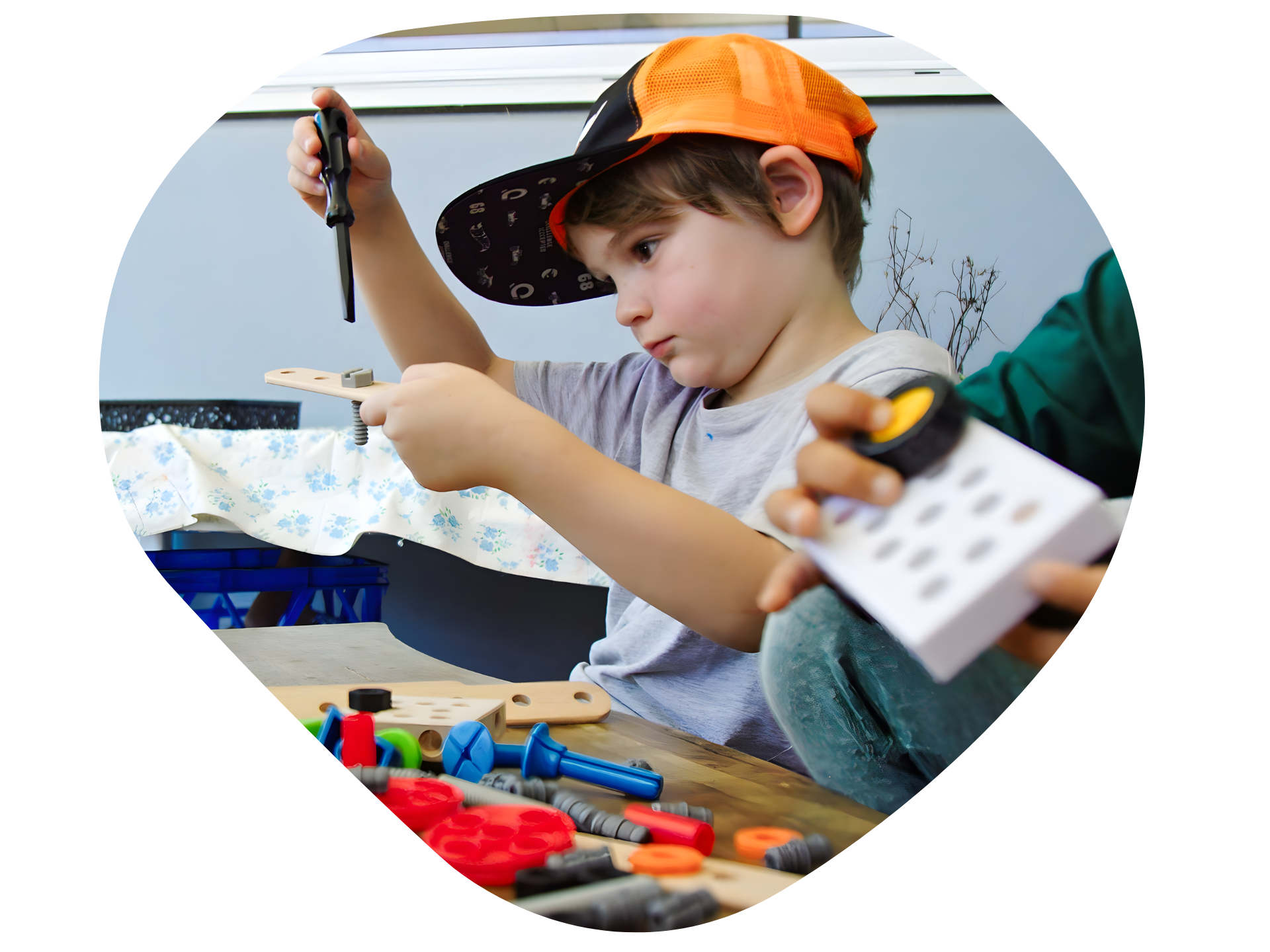 Boy in orange cap, focused on building with various colored parts at a table.