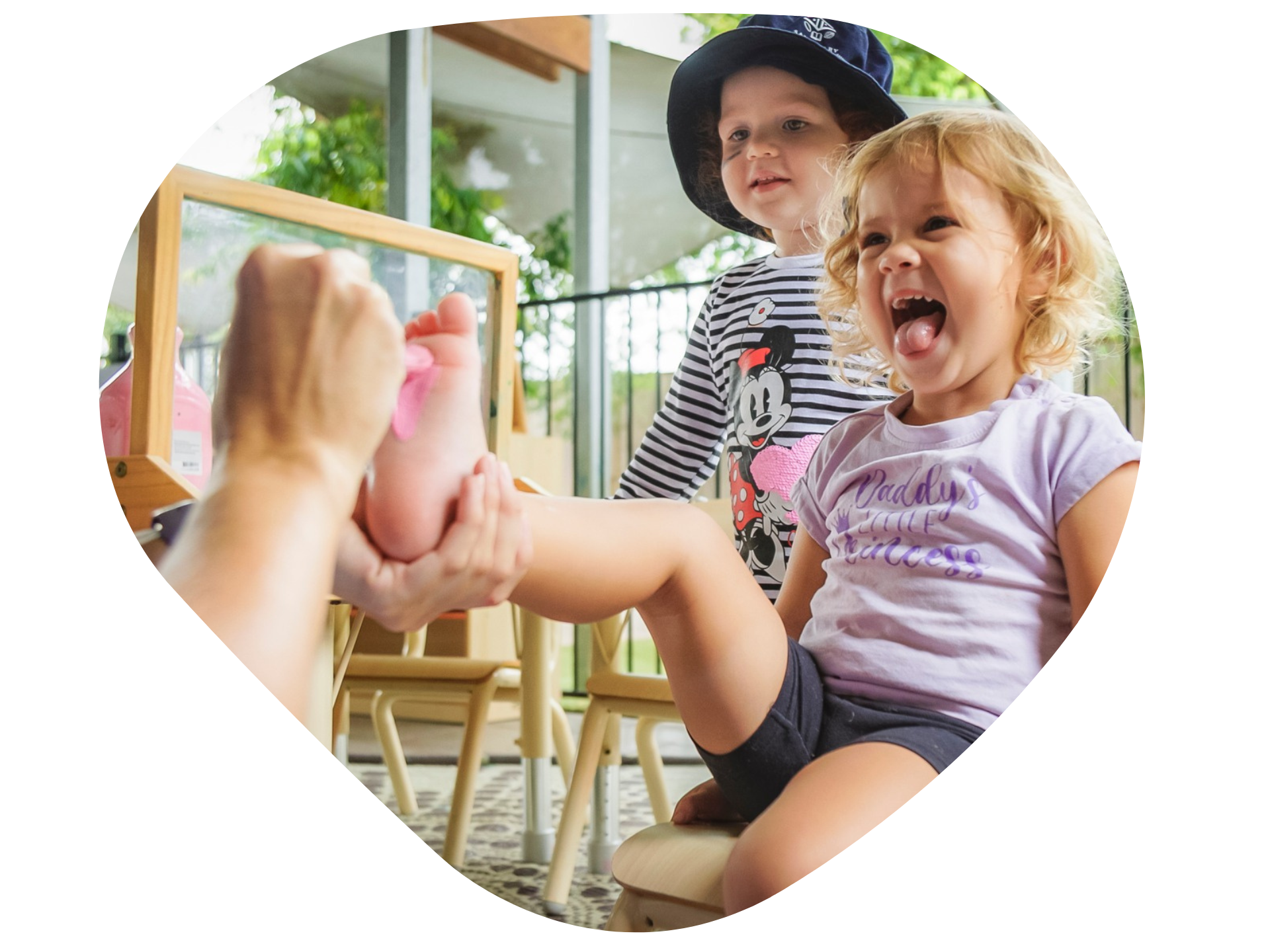 Child getting their foot painted, with another child smiling and observing.