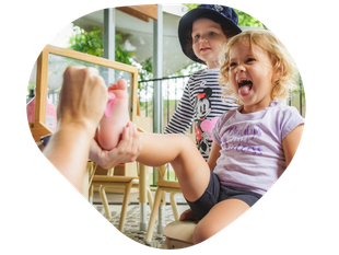 Child getting their foot painted, with another child smiling and observing.