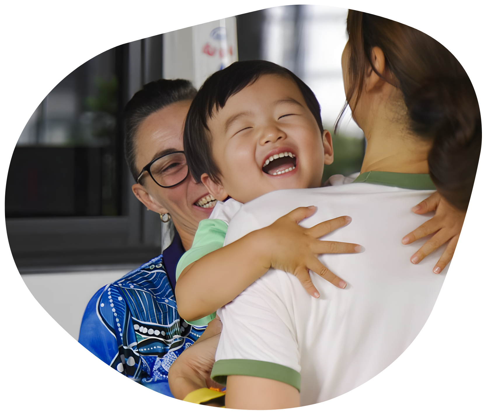 Child laughing while being hugged by an adult, another adult smiling nearby.