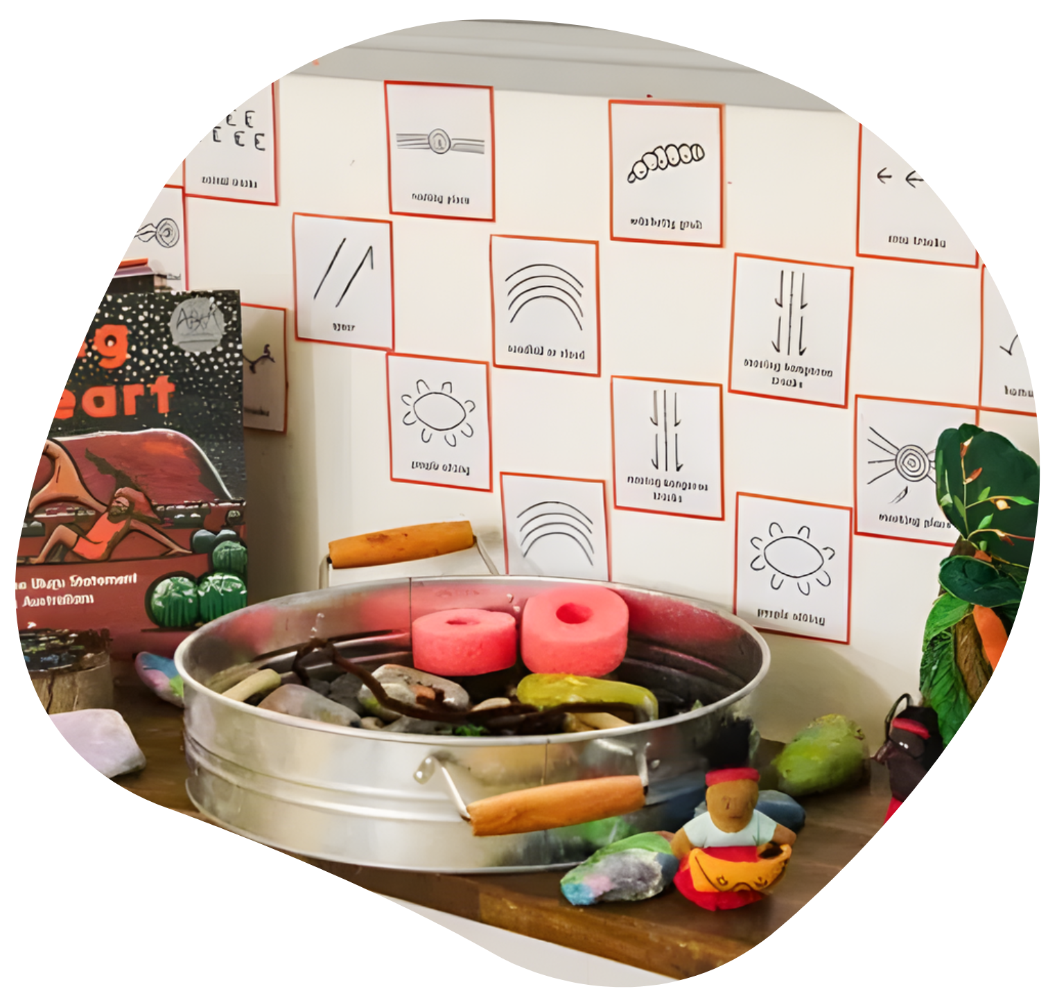 Rocks and colorful objects in a tin, with drawings on the wall. Book and other objects on a wooden surface.