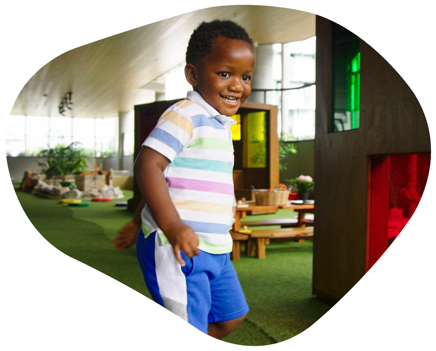 Smiling child in striped shirt and blue shorts, running in a colorful indoor playspace.