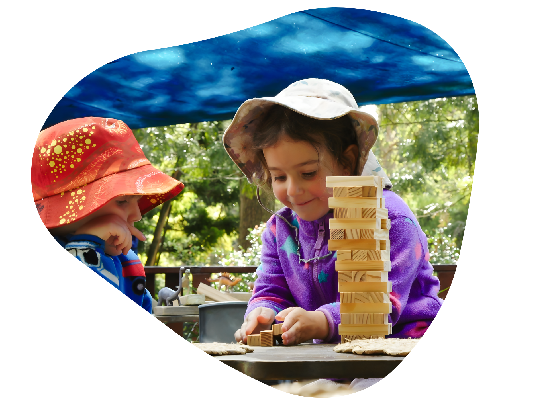 Two children playing Jenga outdoors under a blue canopy.