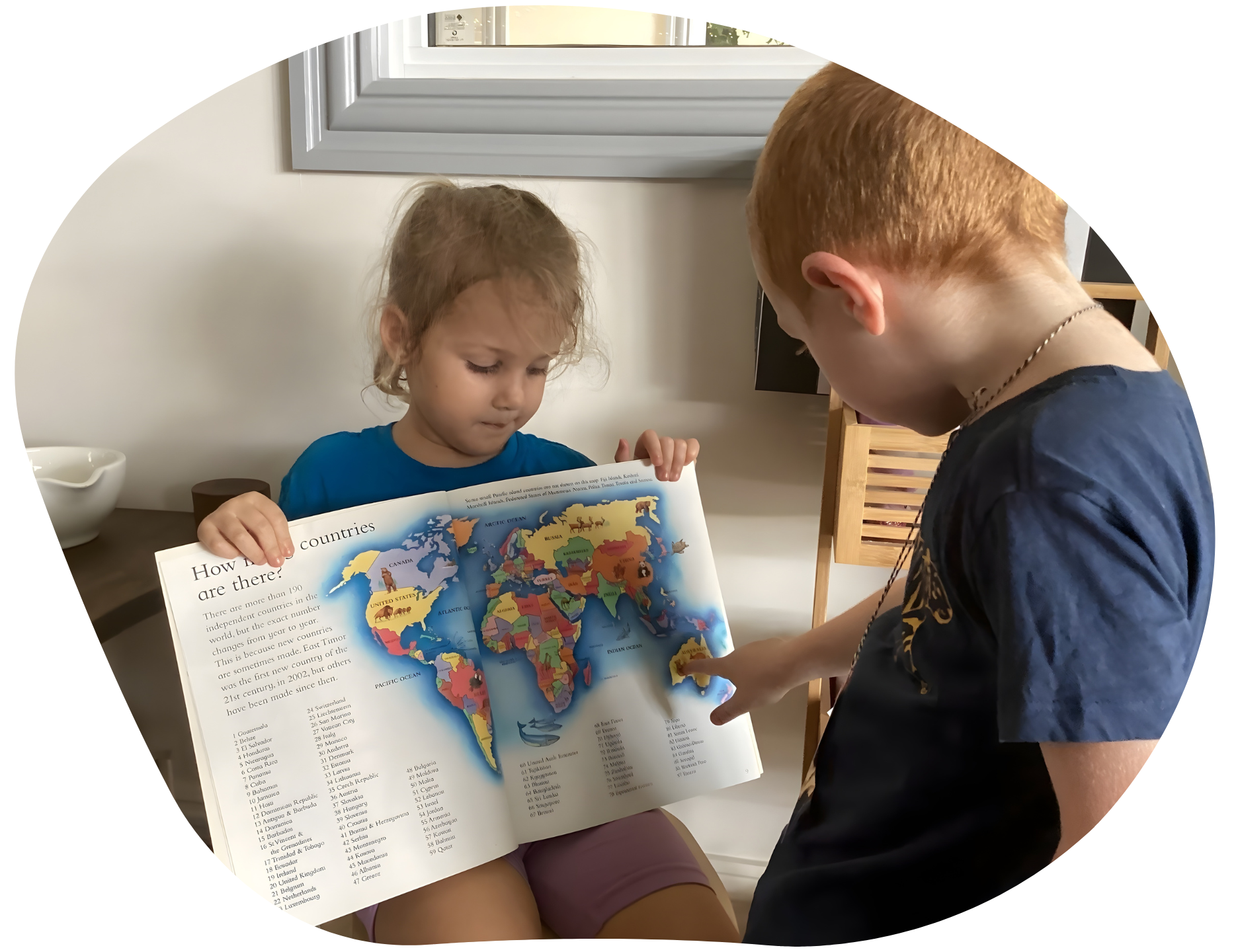Two children looking at a colorful world map. One points to the map while the other holds it.