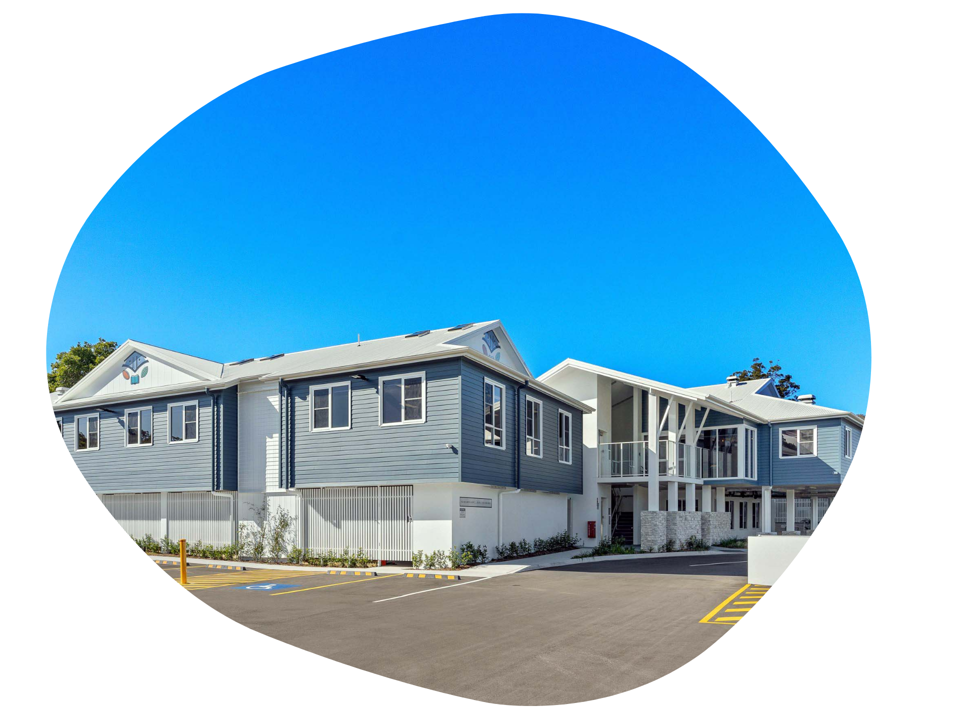 Two-story blue and white building with several windows and a parking lot, against a clear blue sky.